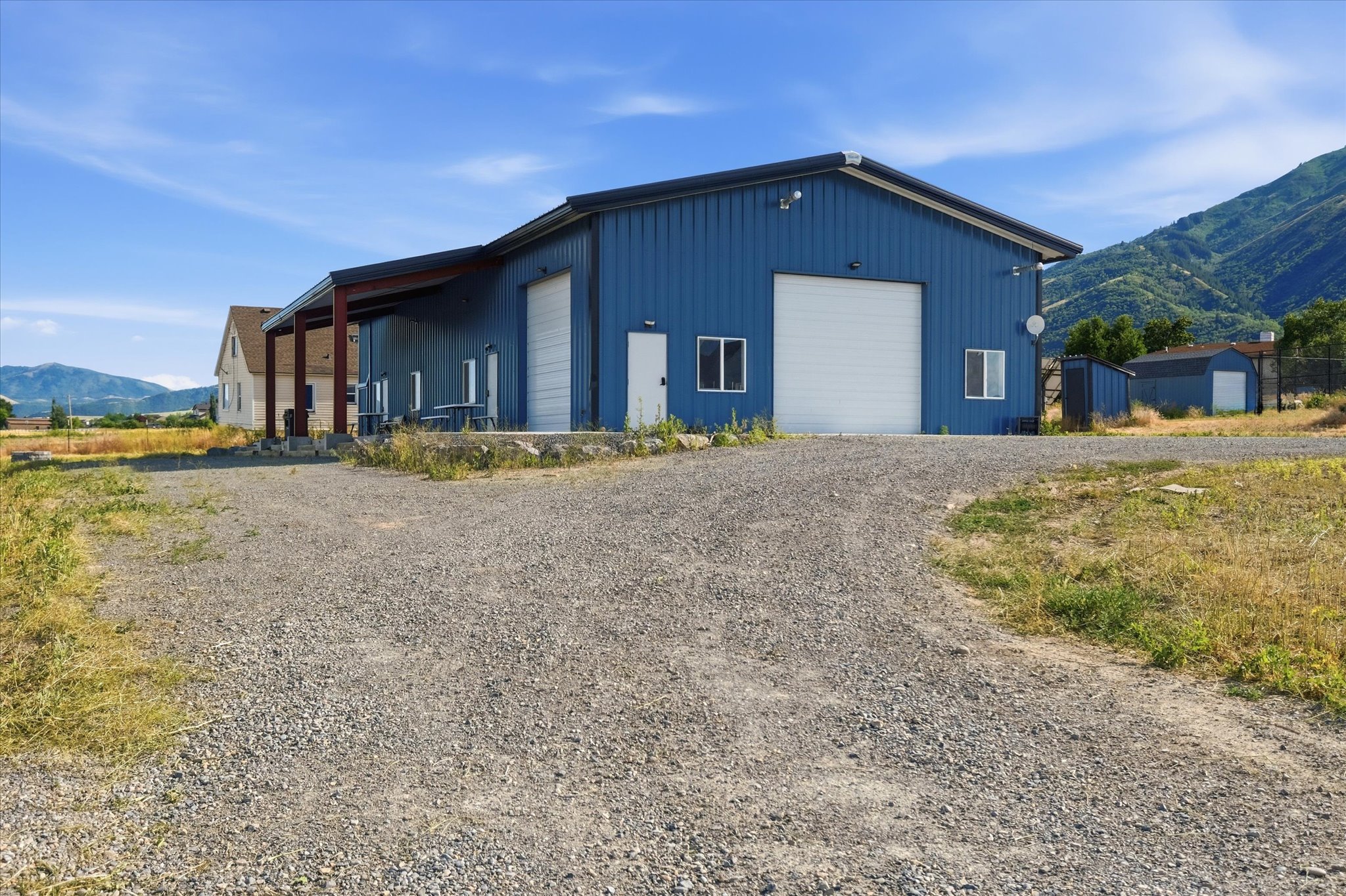 Blue metal-sided structure featuring two white garage doors, multiple exterior windows, and a covered side patio