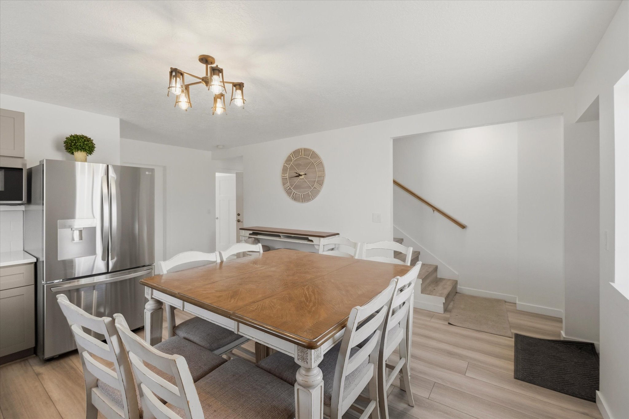 Open-concept living space featuring wood-finish flooring, a contemporary chandelier, and a stainless steel refrigerator