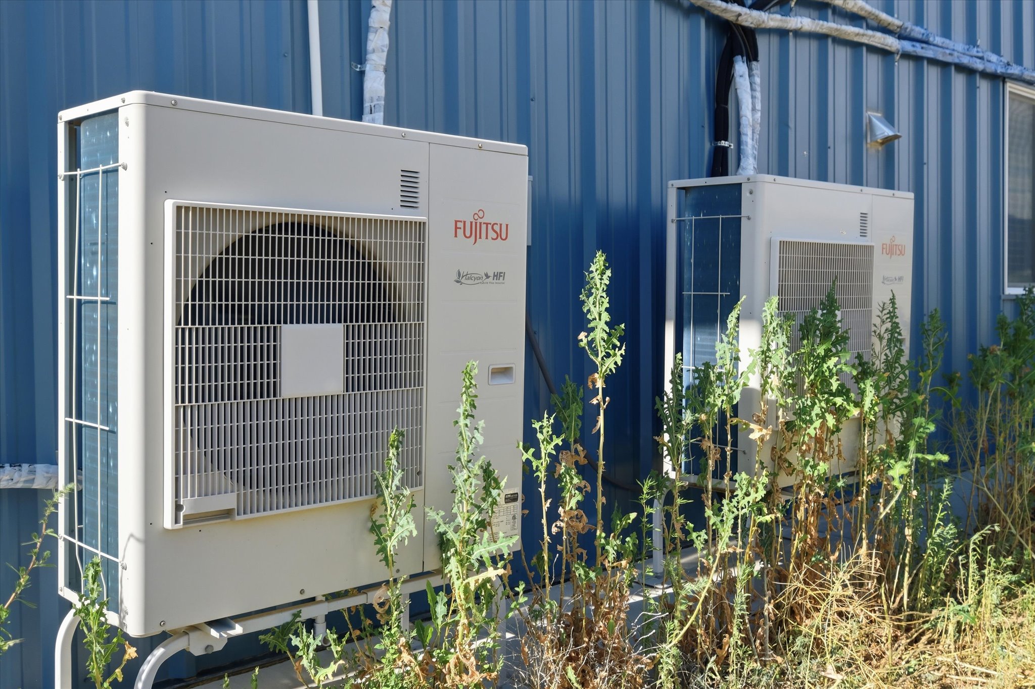 Two Fujitsu outdoor HVAC units mounted on a blue corrugated metal building