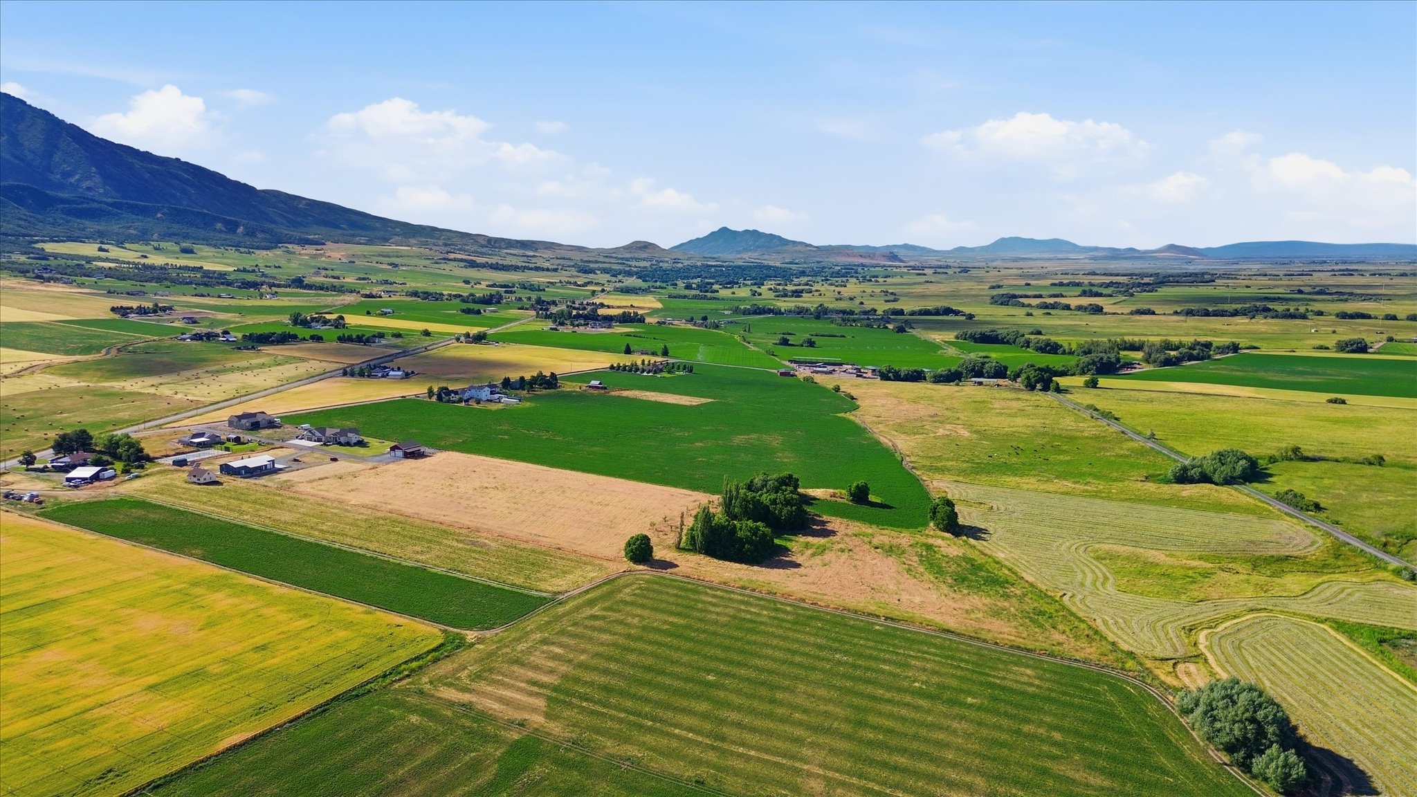 Expansive agricultural landscape featuring diverse cultivated fields, distant mountain ranges, and scattered rural structures