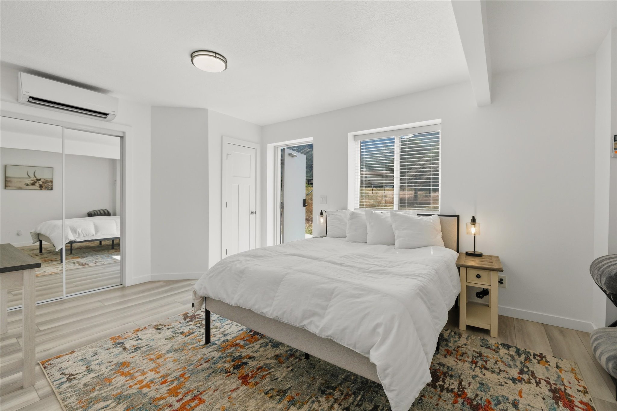 Bright sleeping area featuring wood-finish flooring, white walls, and a large window with blinds