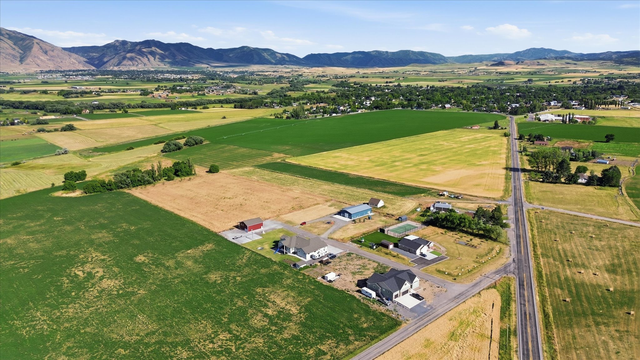 Expansive rural landscape featuring a mix of agricultural fields and scattered residential properties, bordered by distant mountains