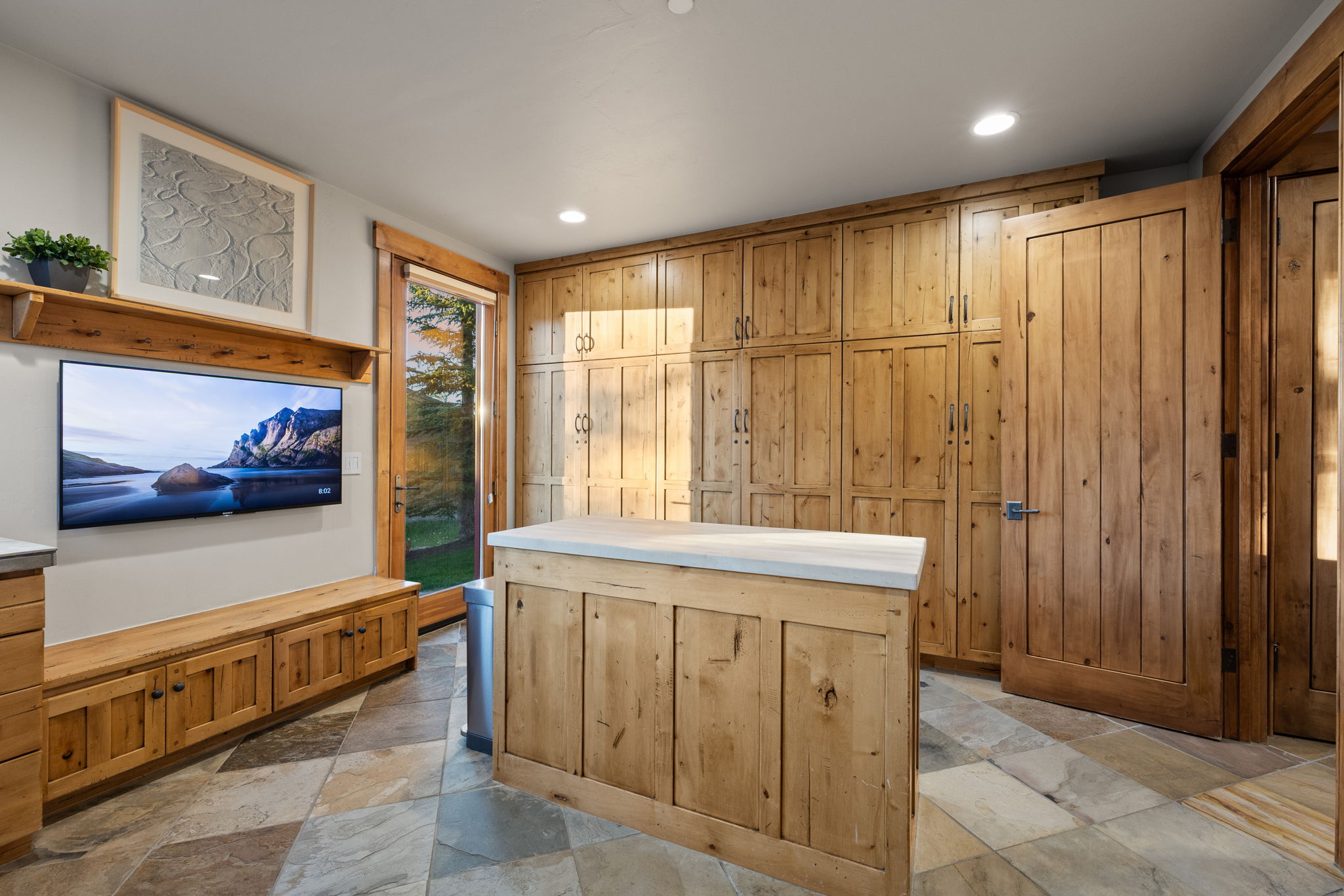 Room featuring extensive wood-finish cabinetry, an entertainment center with built-in storage, a central island with a light-toned countertop, and natural stone tile flooring
