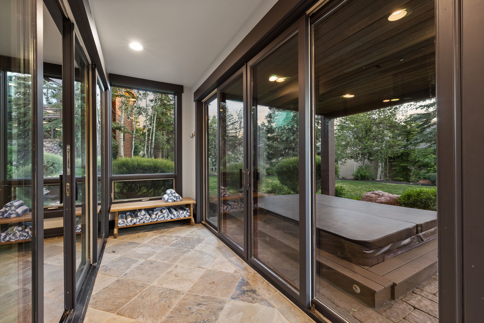 Enclosed patio with full-height sliding glass doors and transom windows, featuring stone tile flooring and recessed ceiling lighting