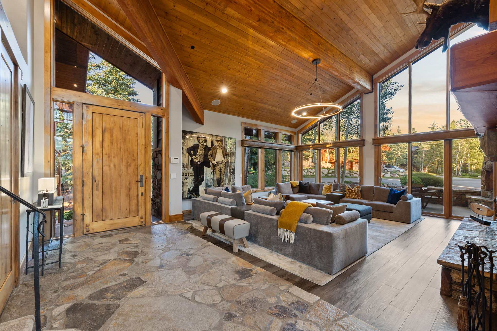 Vaulted wood-paneled ceilings with exposed beams, expansive floor-to-ceiling windows, natural stone flooring, and a solid wood entry door