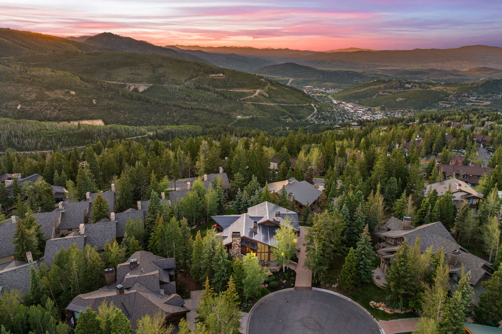 Mountain valley setting with a prominent residence featuring a multi-gabled roofline and extensive tree coverage