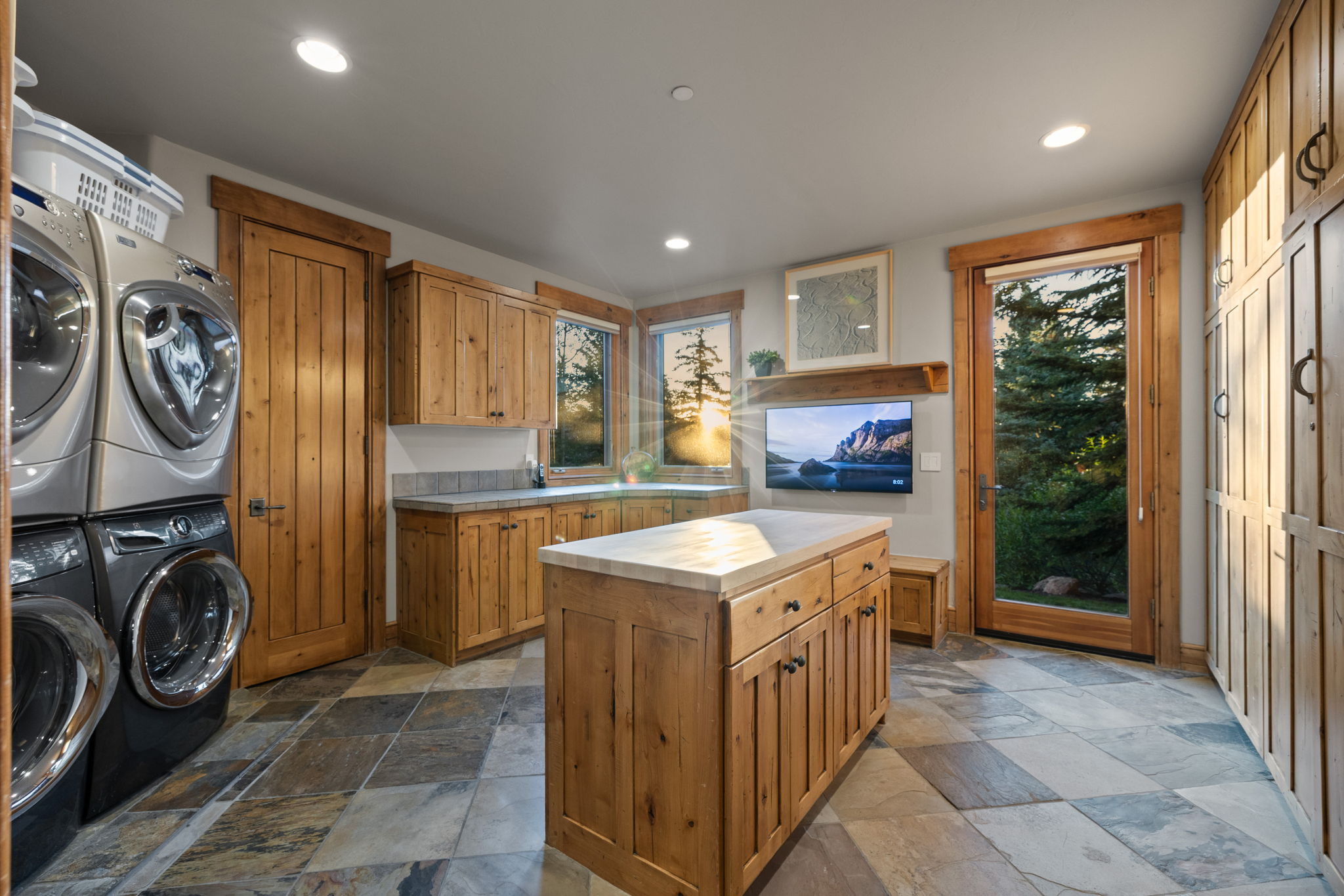 Spacious utility room featuring stacked laundry machines, extensive wood cabinetry, a central island with a solid surface countertop, and slate tile flooring