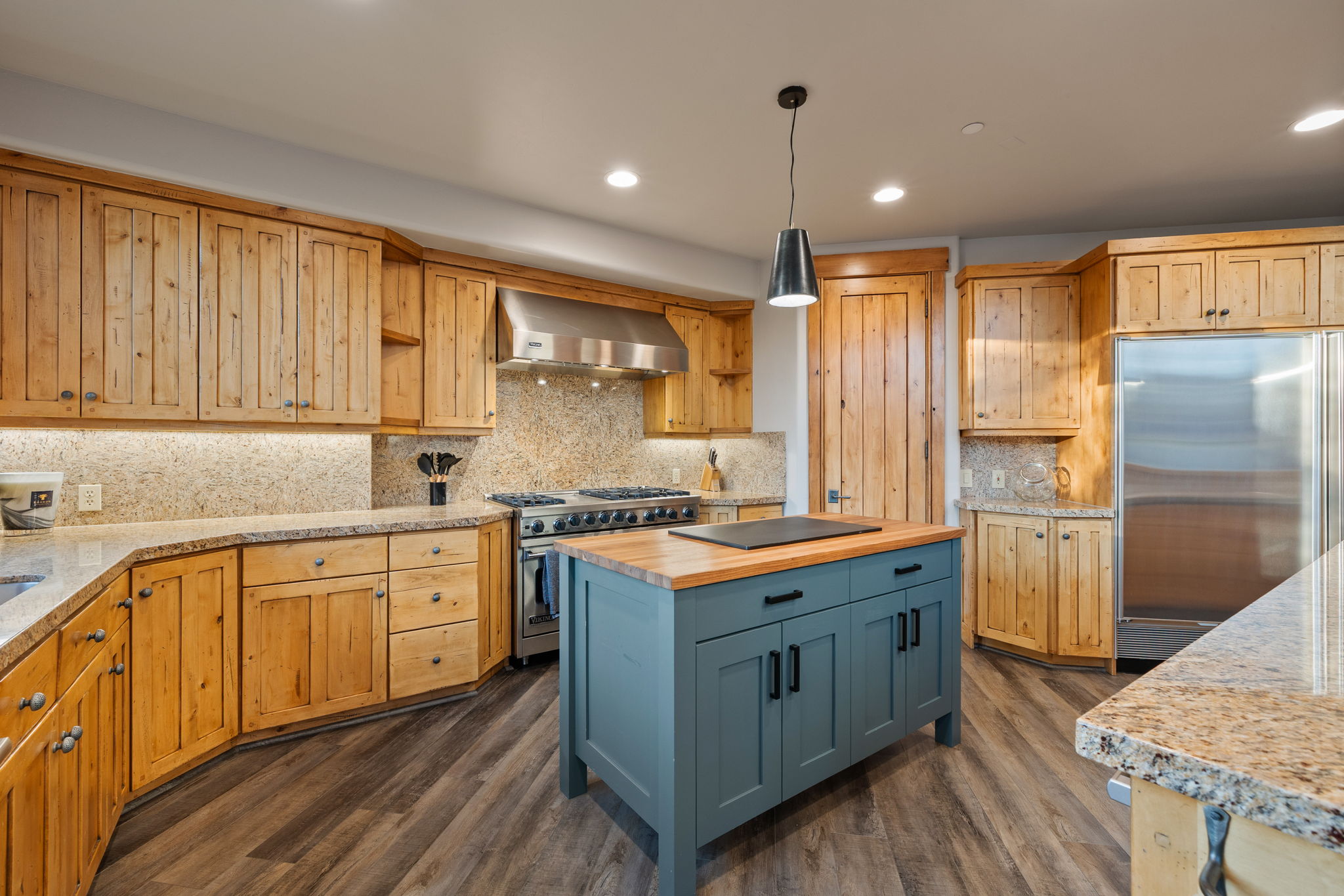 Spacious kitchen featuring natural wood cabinetry, granite countertops, stainless steel appliances, and a central island with a wood-finish top