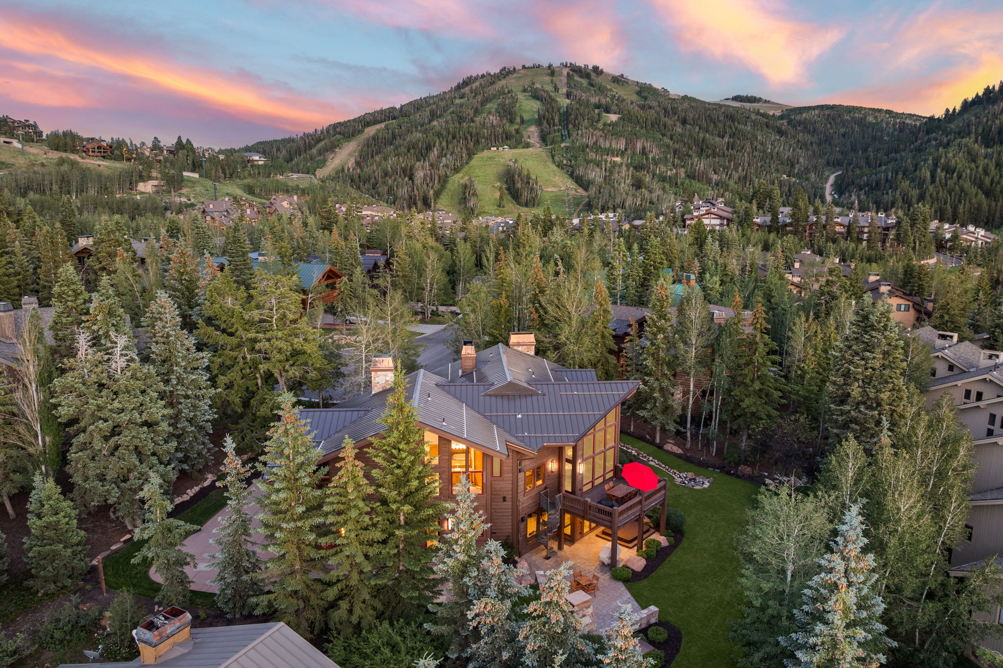 Modern mountain architecture featuring a multi-level deck, expansive windows, a manicured lawn, and mature evergreen trees