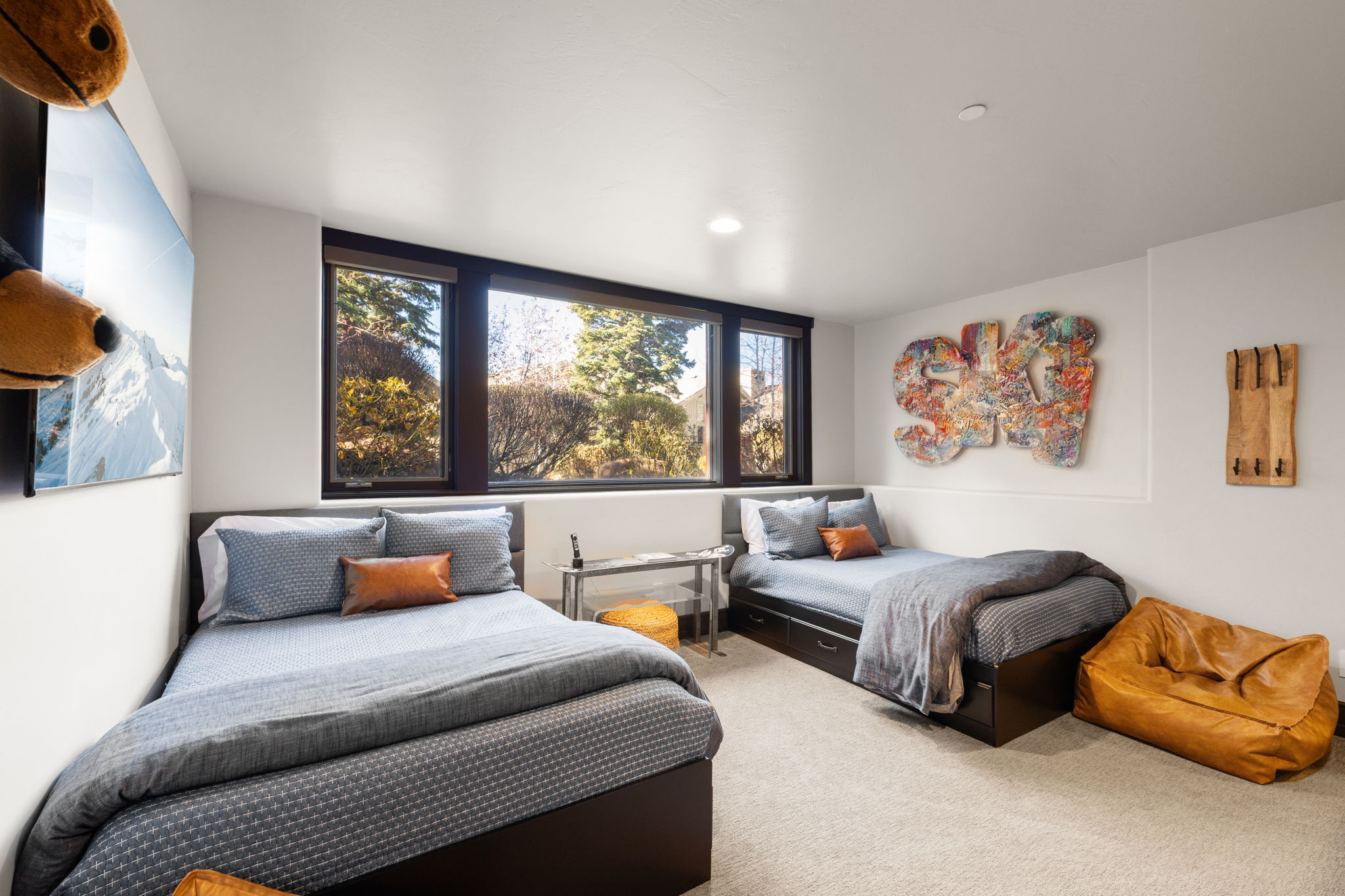 Light-filled room featuring two beds with integrated storage, dark-framed windows, and neutral carpeting