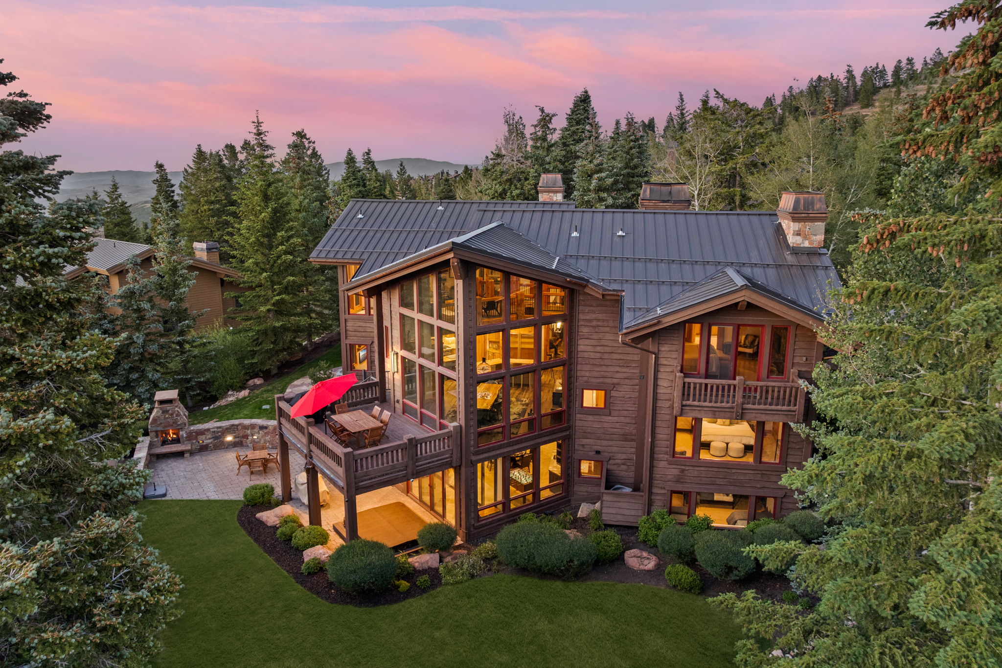 Mountain-style residence featuring a dark metal roof, multiple stone chimneys, extensive wood siding, and multi-level decks
