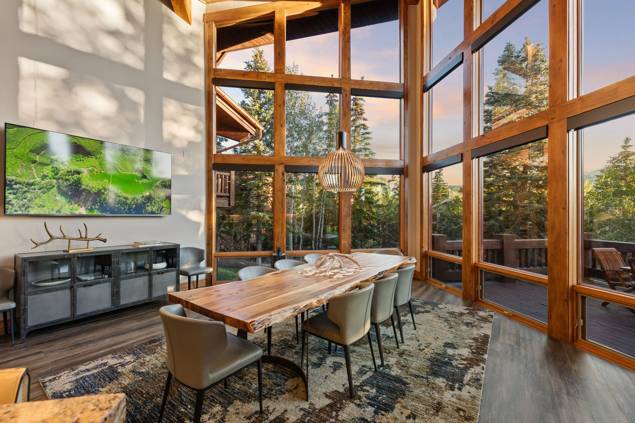 Dining area featuring a full-height wall of expansive windows with natural wood framing, exposed wood beams, wood-finish flooring, and a contemporary pendant light fixture