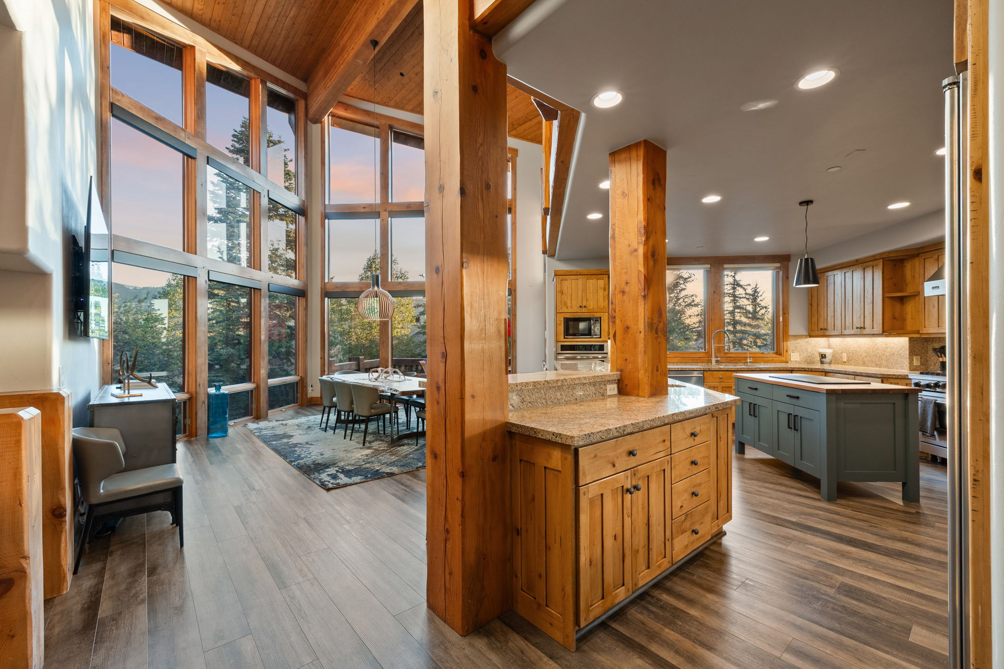 Vaulted ceiling with exposed wood beams, extensive floor-to-ceiling windows, wood-finish flooring, full kitchen with center island, and granite countertops