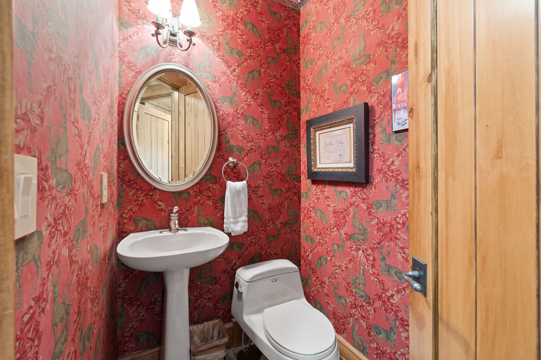 Pedestal sink with chrome faucet, an oval mirror, and wall-mounted vanity lighting
