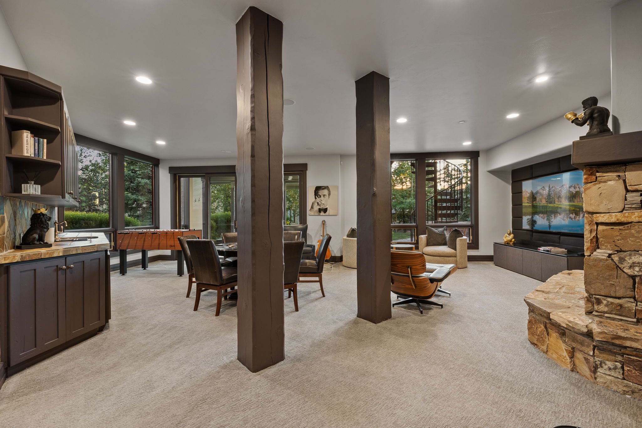 Lower level entertainment space featuring a natural stone fireplace, a wet bar with dark wood cabinetry and a stone countertop, and recessed lighting