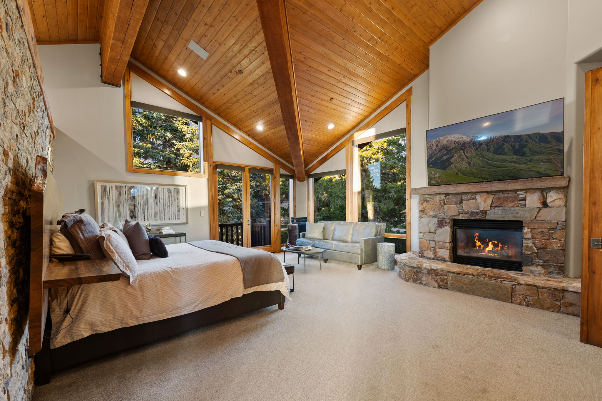 Vaulted wood-paneled ceiling with exposed beams, stone fireplace, and large picture windows