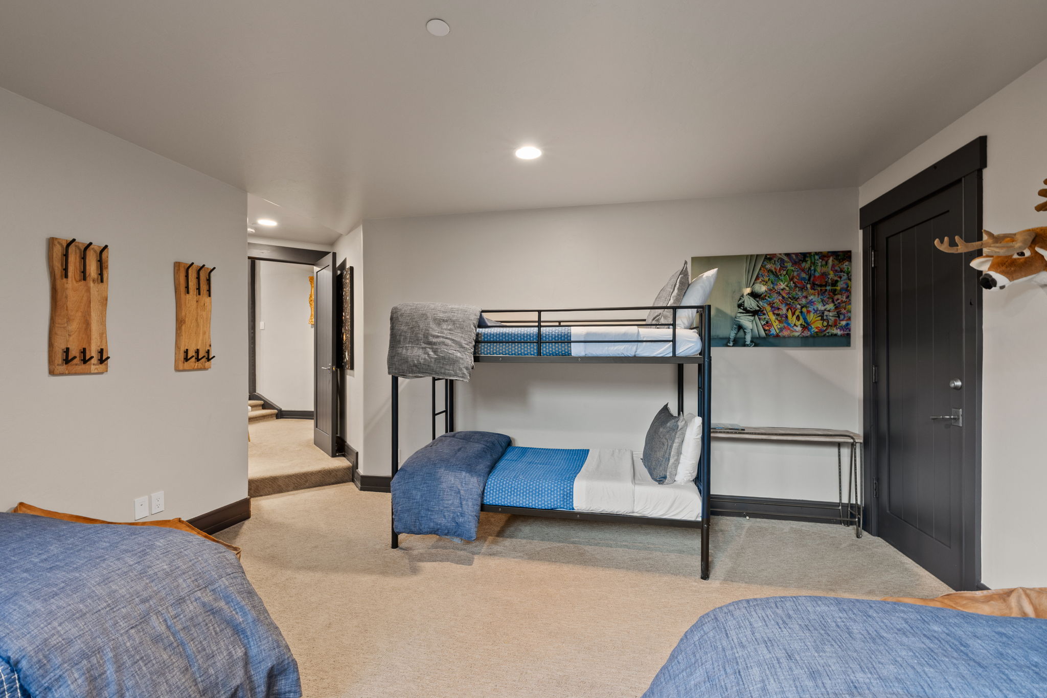 Spacious room with plush carpeting, recessed lighting, a modern bunk bed frame, a dark paneled door, and two wood wall-mounted coat racks