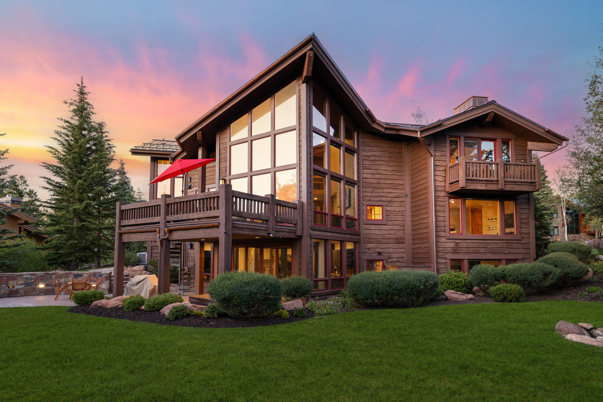 Contemporary timber-frame residence featuring expansive window walls, multiple balconies, a stone patio, and a manicured lawn