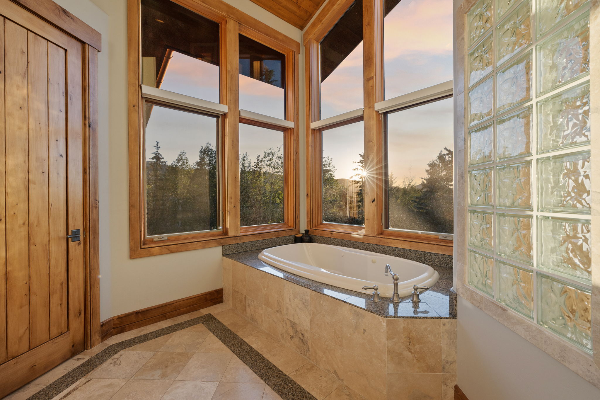 Corner soaking tub with a granite surround, set against a wall of wood-framed windows