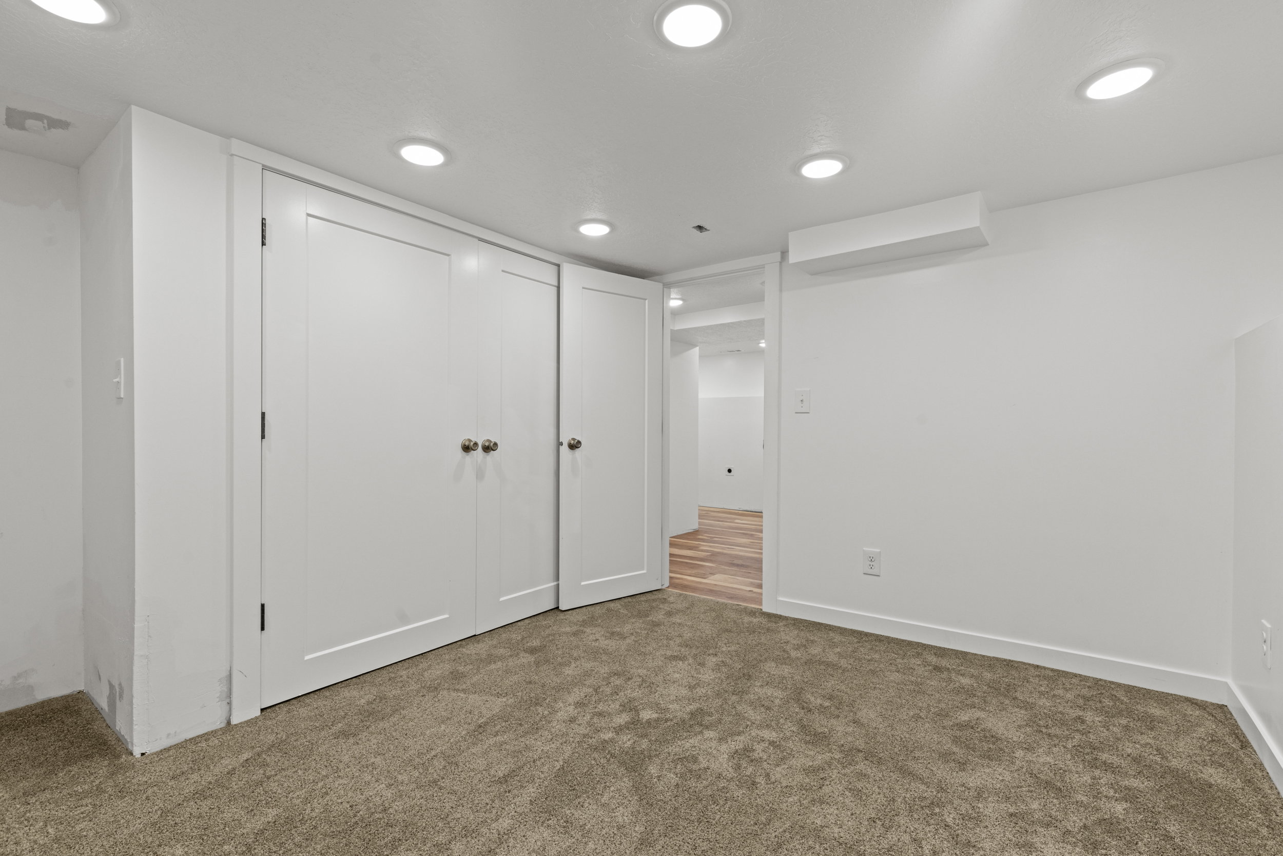 Carpeted room featuring multiple recessed ceiling lights, white walls, and white bi-fold closet doors with round brushed nickel hardware