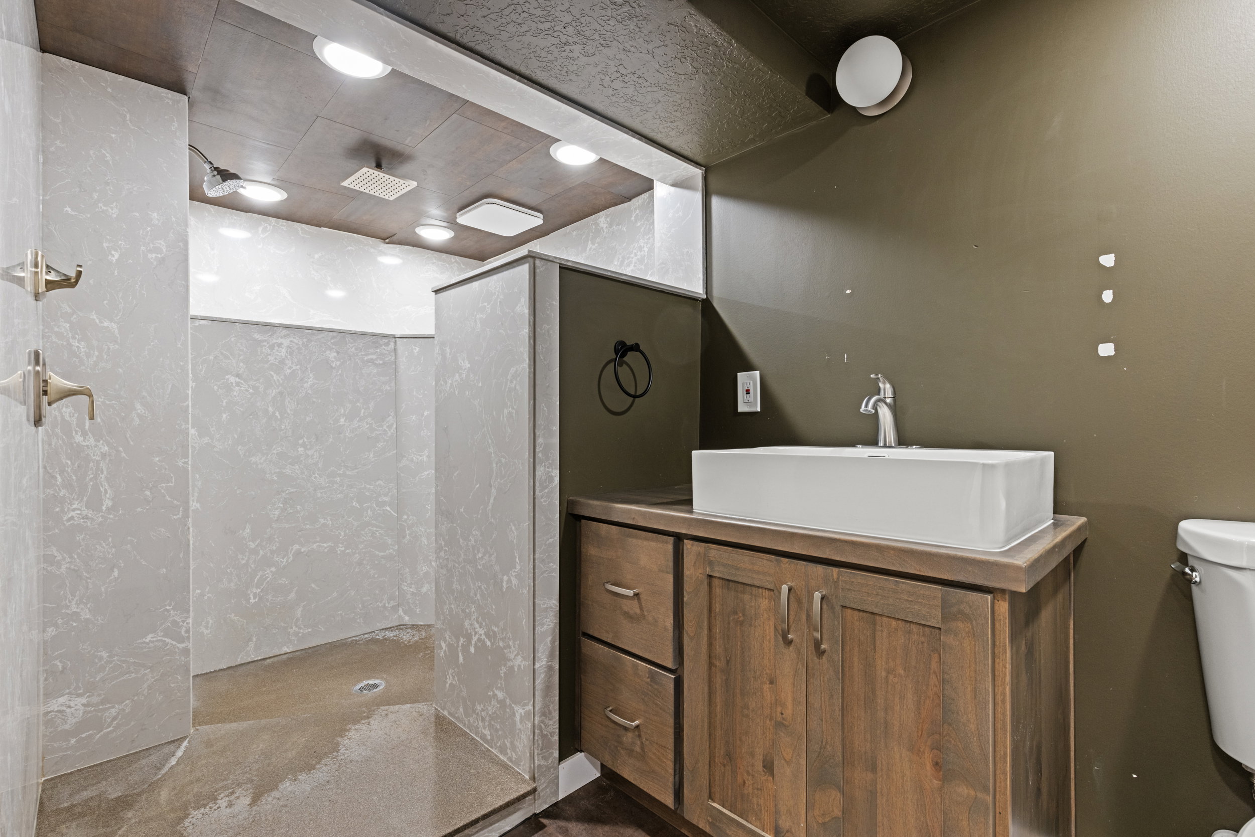 Spacious walk-in shower with light-toned, marble-patterned walls and a wood-finish ceiling featuring recessed lighting
