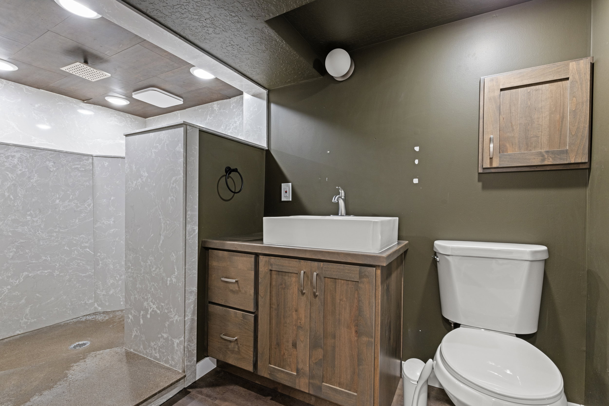 Bathroom featuring a walk-in shower with textured wall panels, a wood-finish vanity with a rectangular vessel sink, a chrome faucet, and a wall-mounted wood-finish cabinet