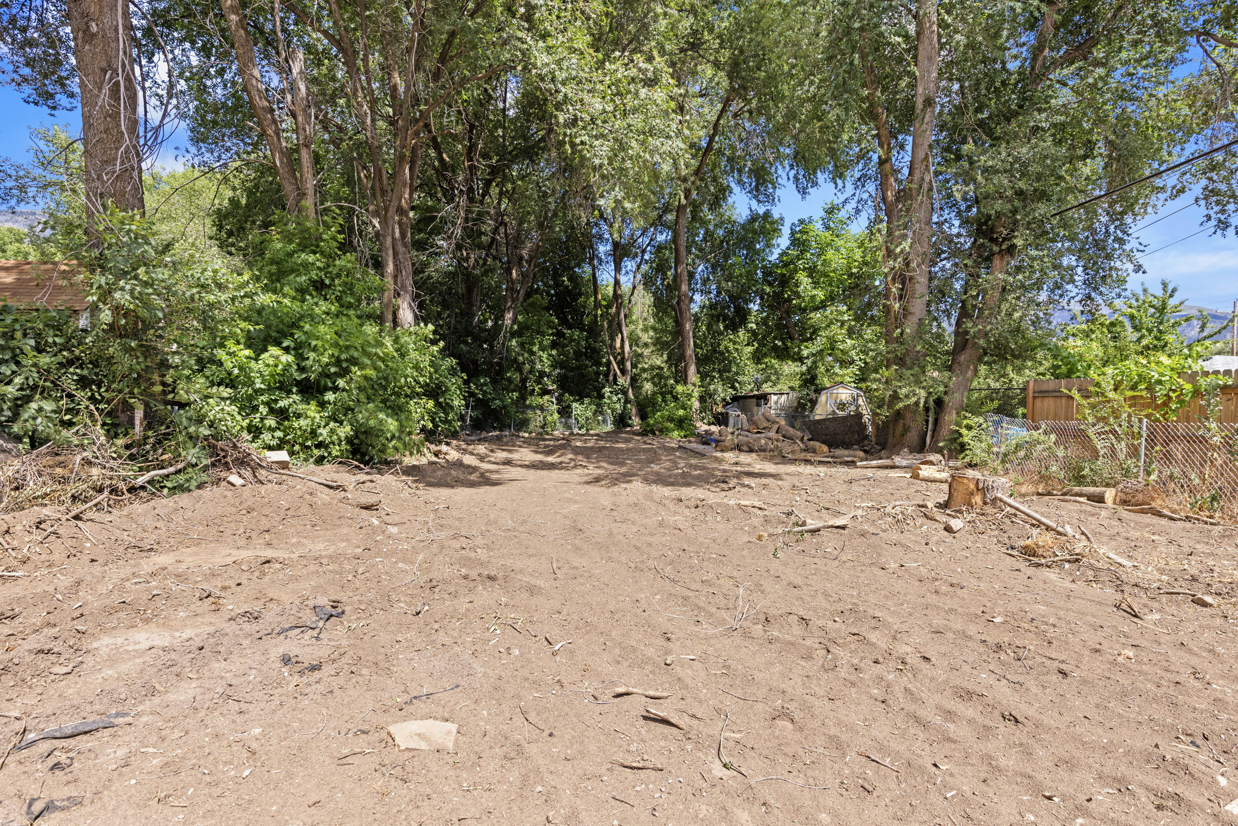 Expansive cleared lot featuring mature trees providing natural shading, perimeter fencing, and a level buildable area