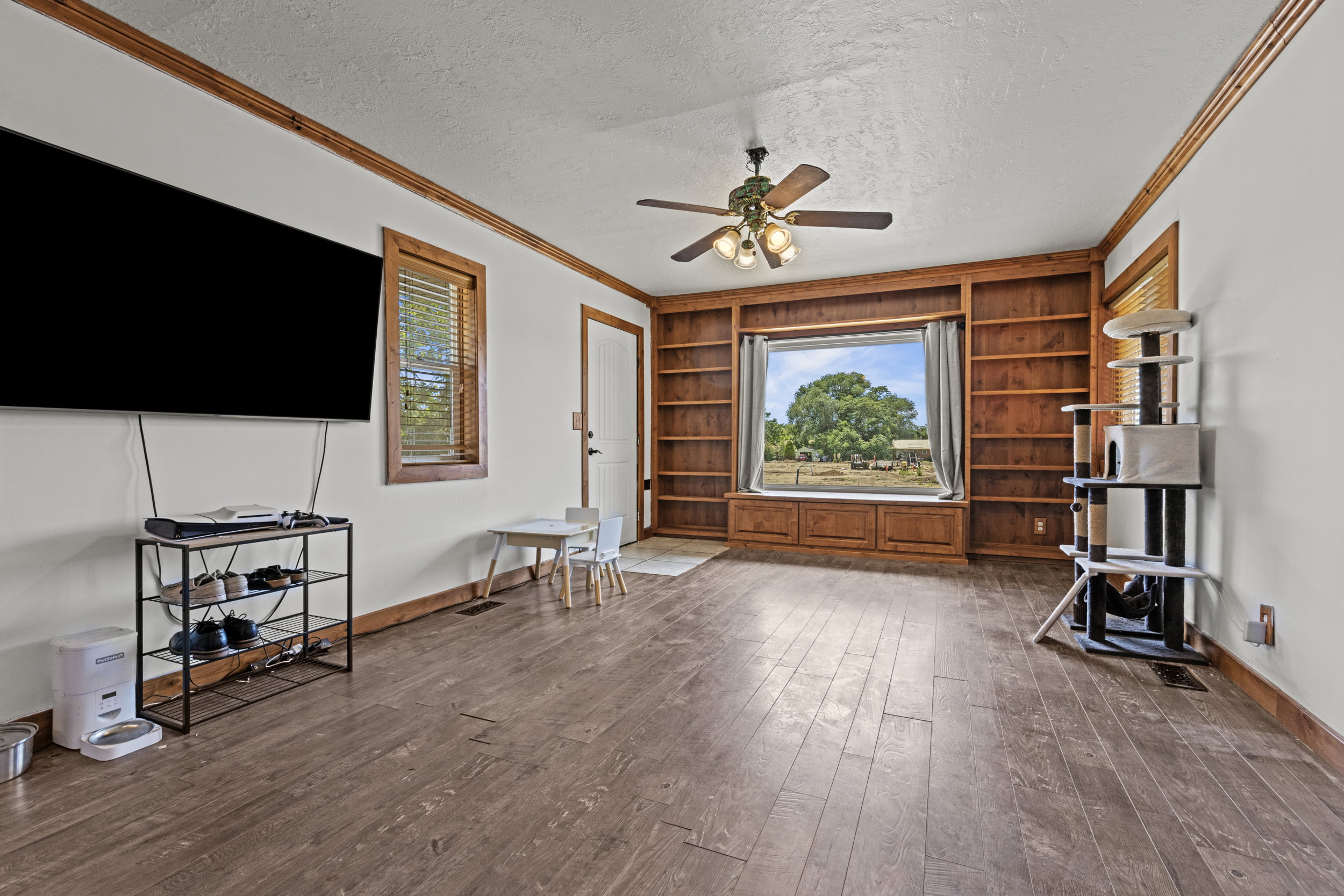 Living area featuring wood-finish flooring, built-in shelving, a window seat with storage, a ceiling fan, and wood trim accents