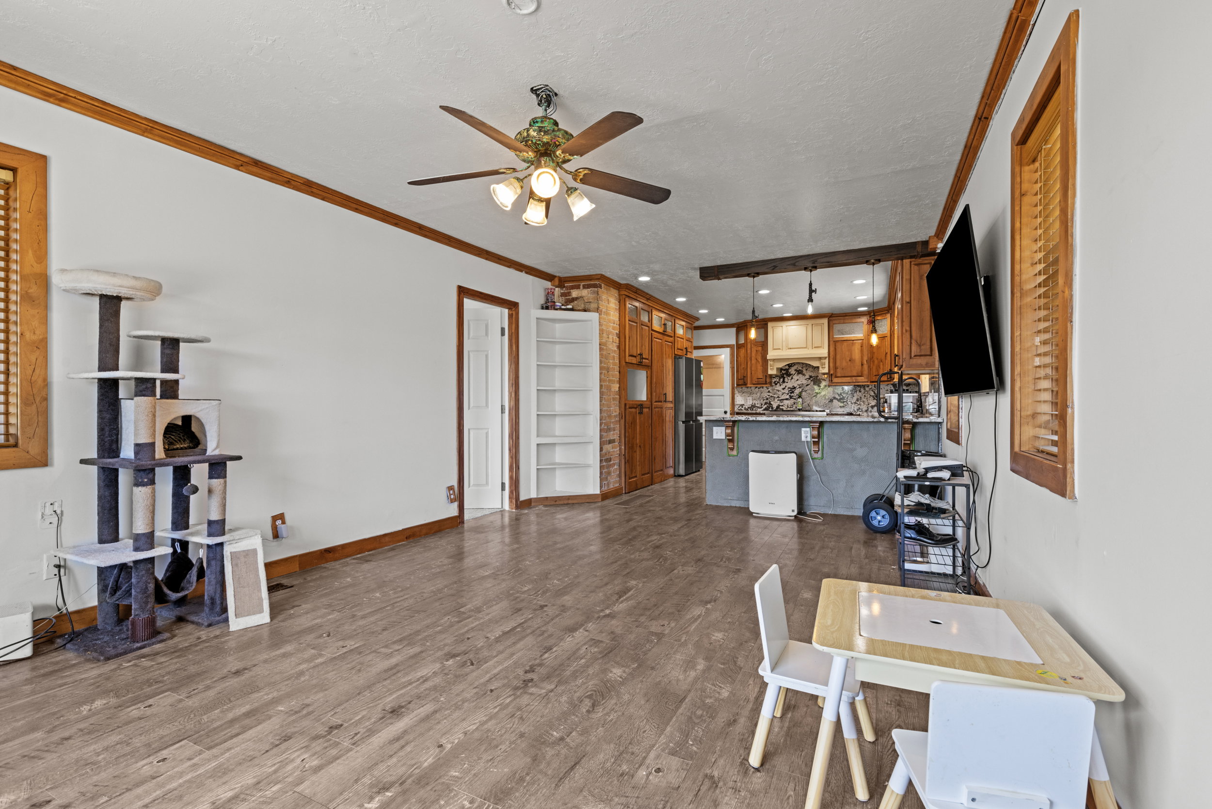 Open-concept living area featuring wood-finish flooring, a ceiling fan with integrated lighting, and white walls with wood trim