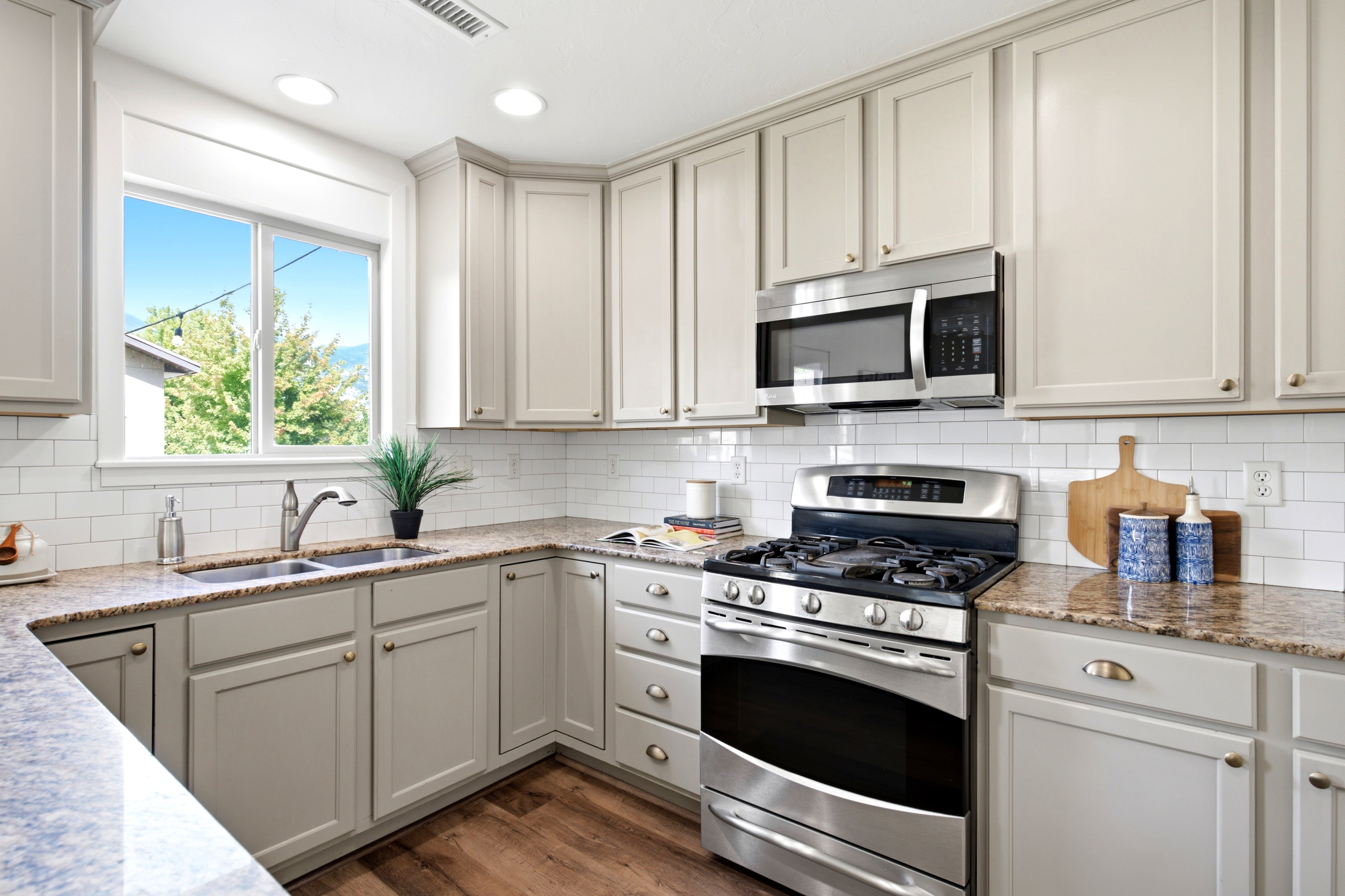Kitchen featuring light-toned cabinetry, granite-finish countertops, stainless steel appliances, a subway tile backsplash, and wood-finish flooring