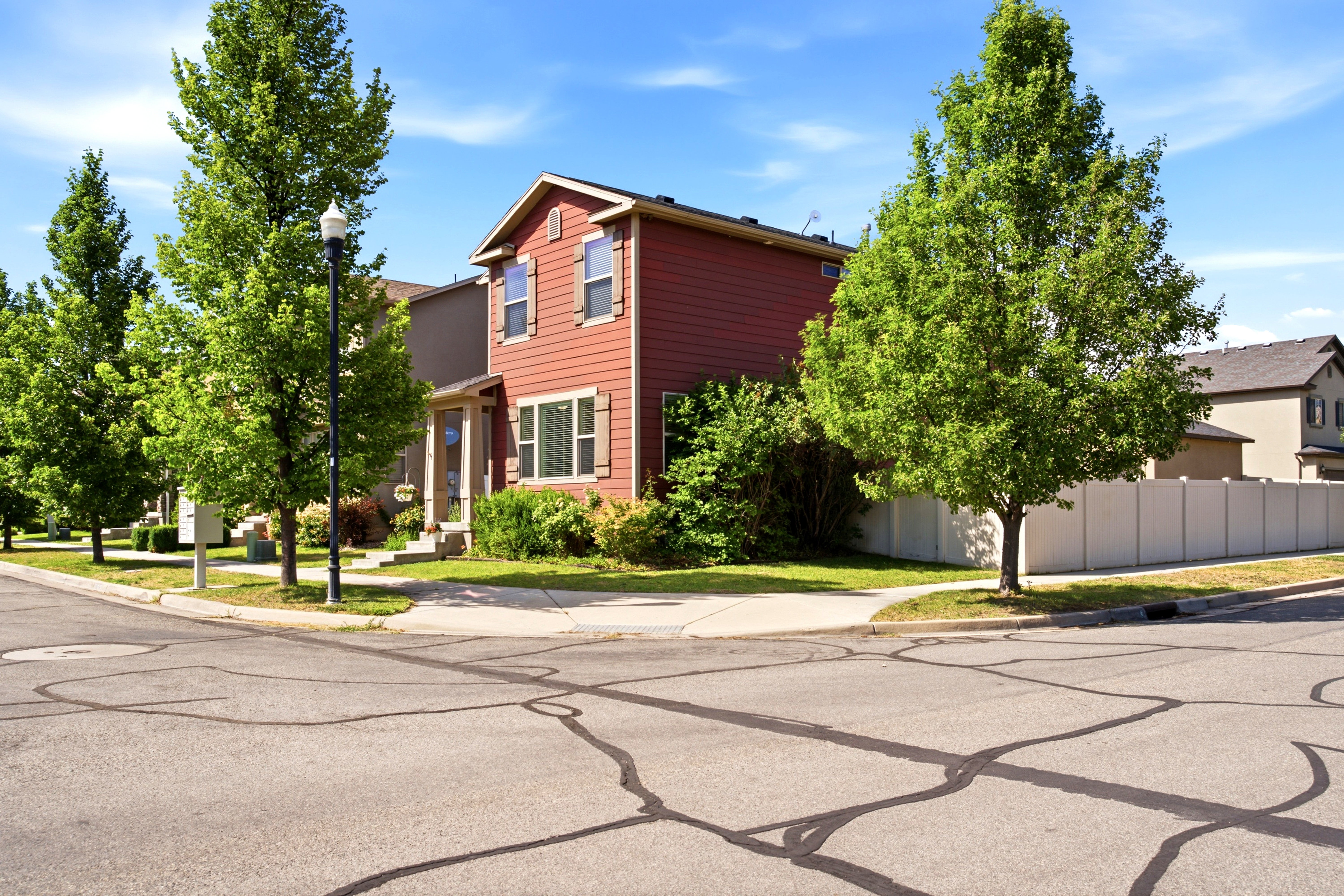 Red siding exterior with contrasting window shutters, mature trees, and a corner lot location