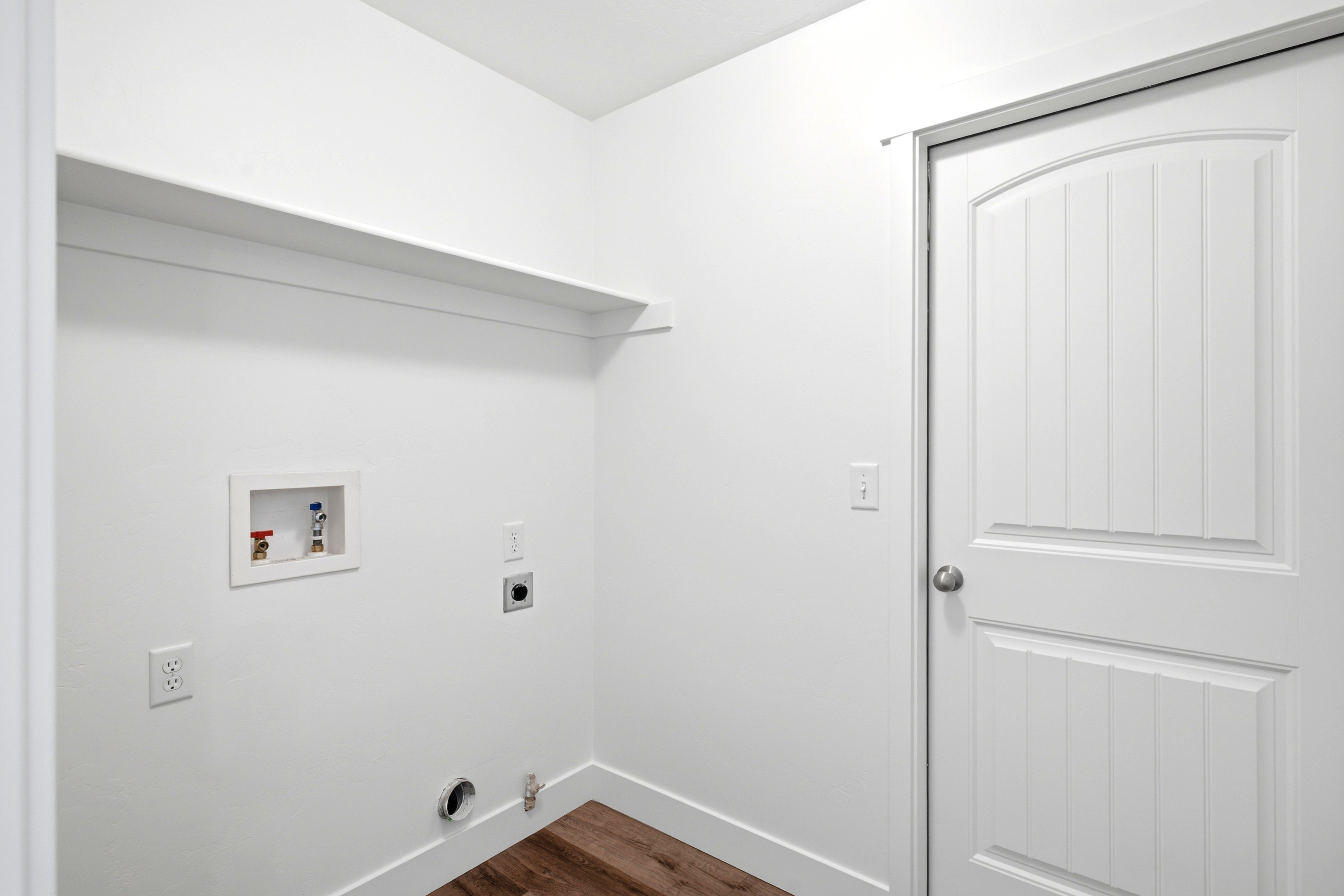 Dedicated laundry area featuring a white storage shelf, wood-finish flooring, and a paneled door