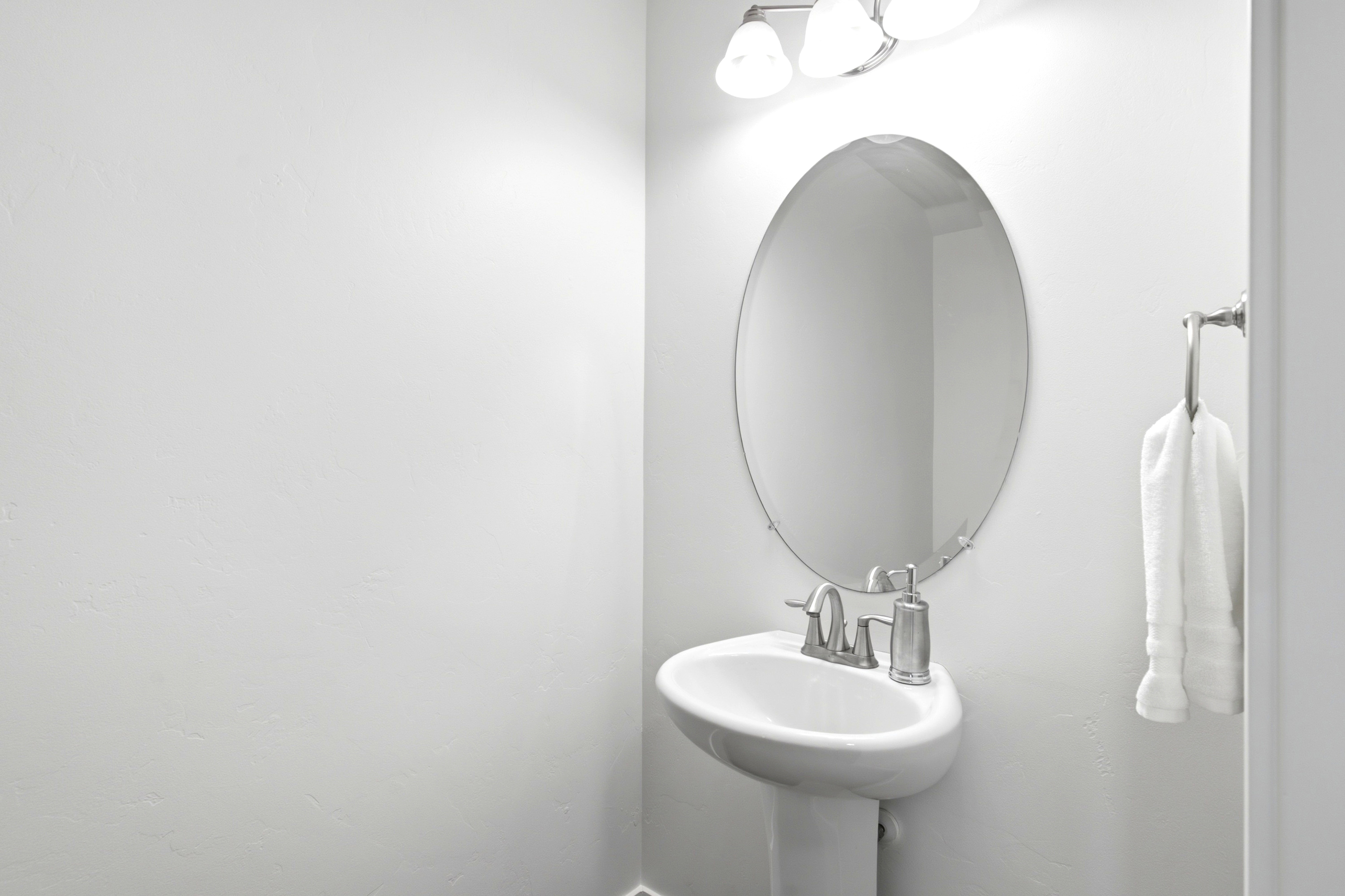 Pedestal sink with a chrome two-handle faucet, an oval mirror, and a three-light vanity fixture