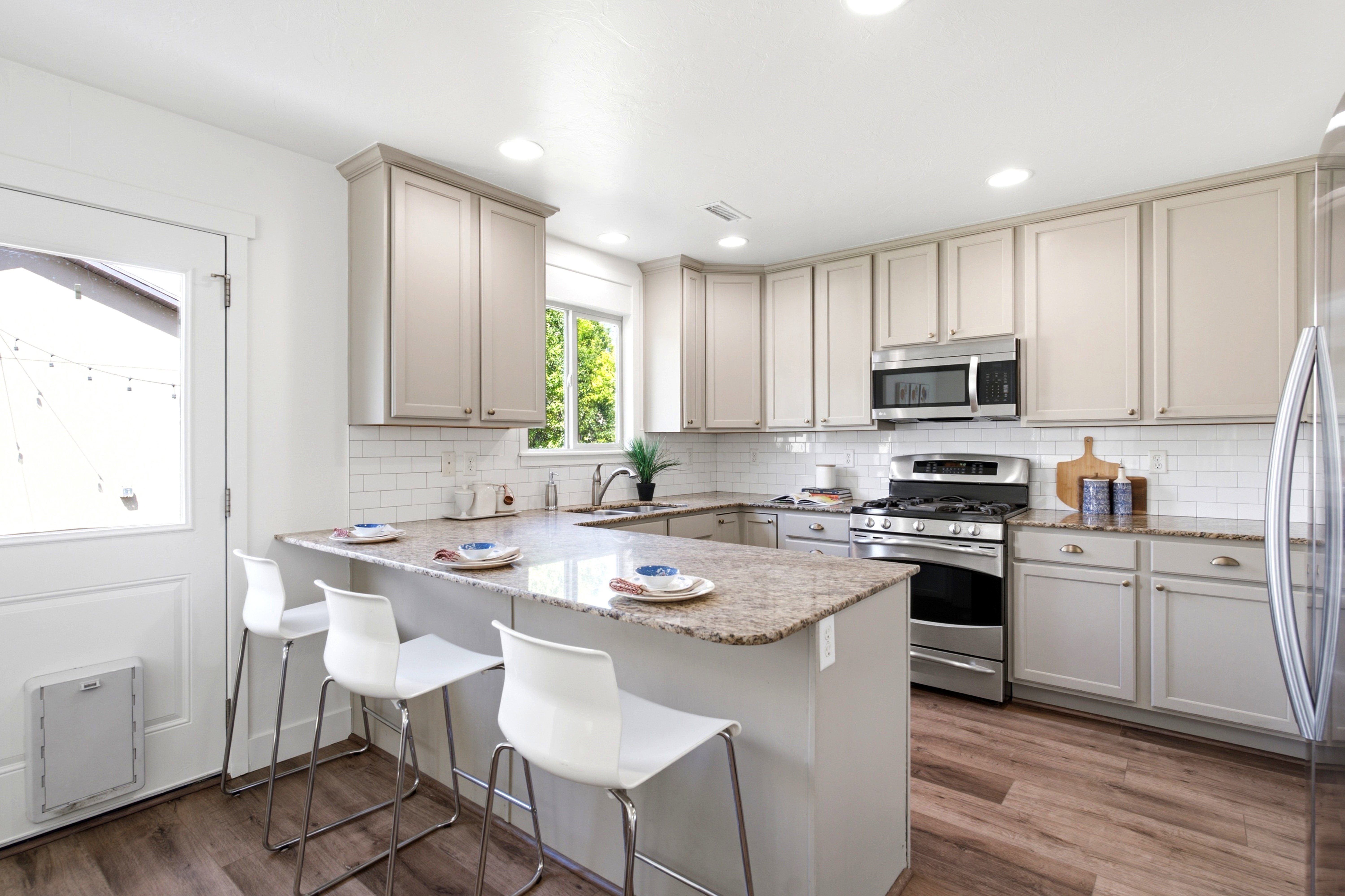 Contemporary kitchen featuring light-toned cabinetry, stainless steel appliances, a white subway tile backsplash, granite countertops, and wood-finish flooring
