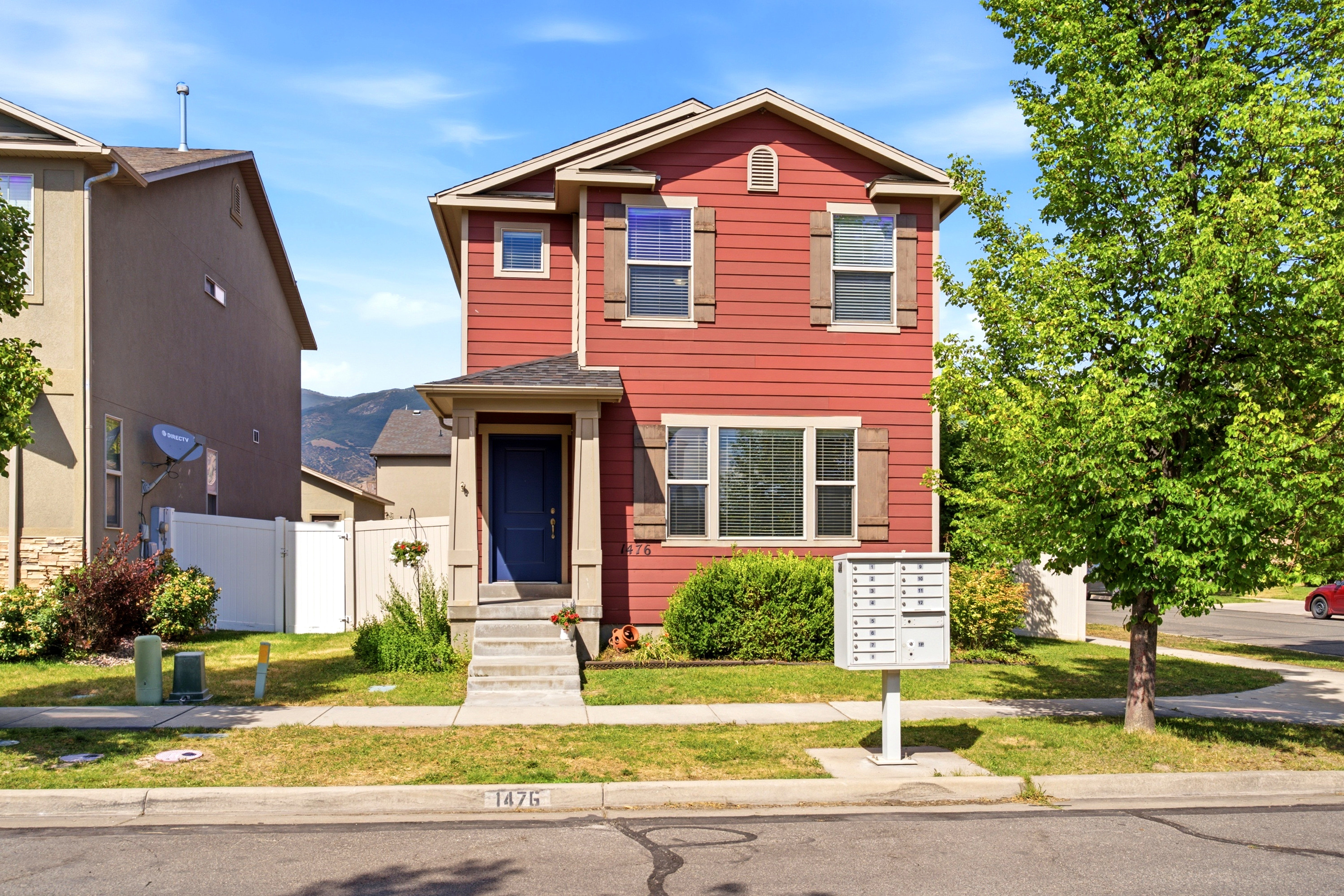 Two-story residence featuring red siding and brown shutters, a covered entry with a blue door, a concrete walkway, and a green lawn