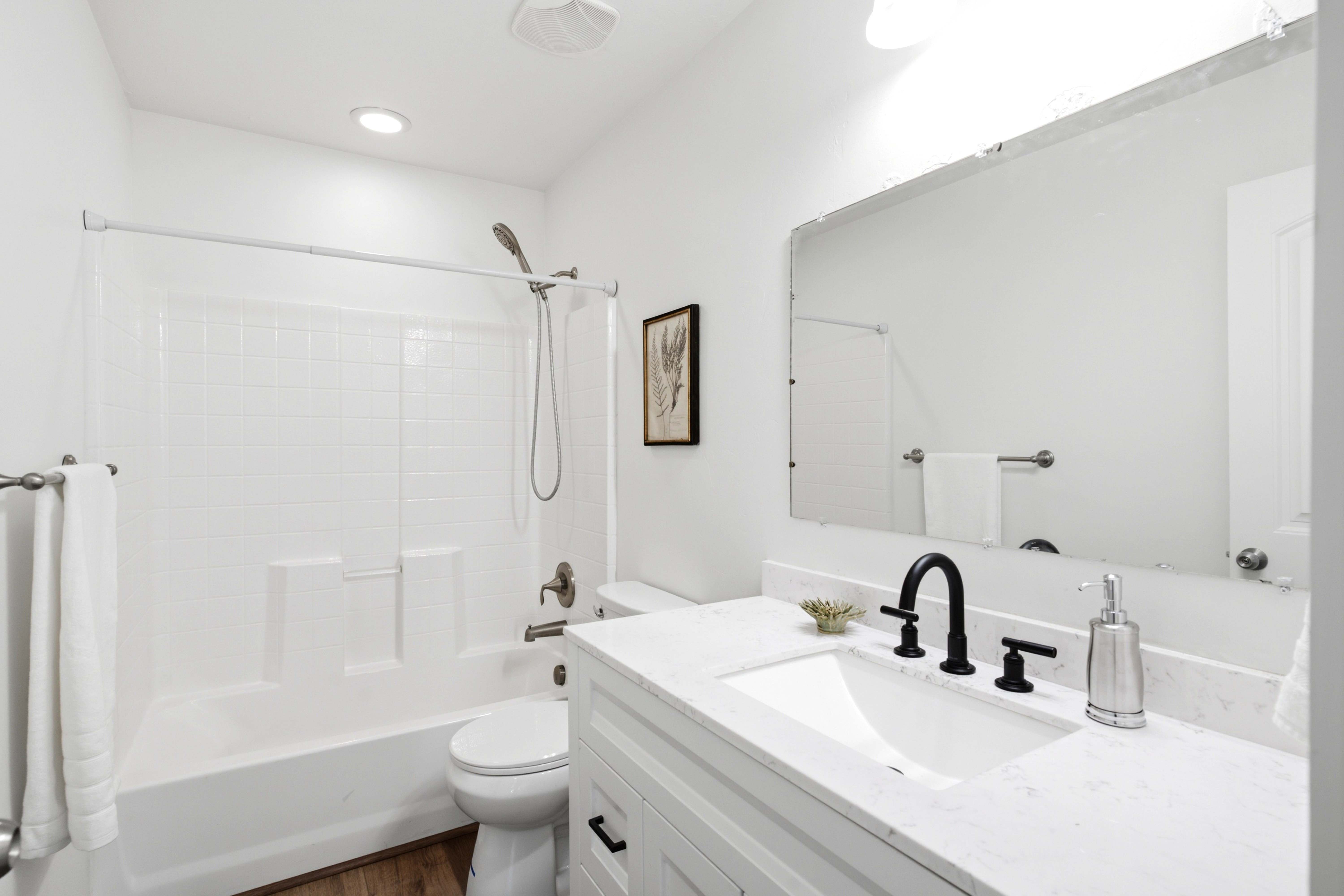 Bathroom featuring a white subway tile shower surround, a white vanity with a light-toned countertop, a black gooseneck faucet, and wood-finish flooring