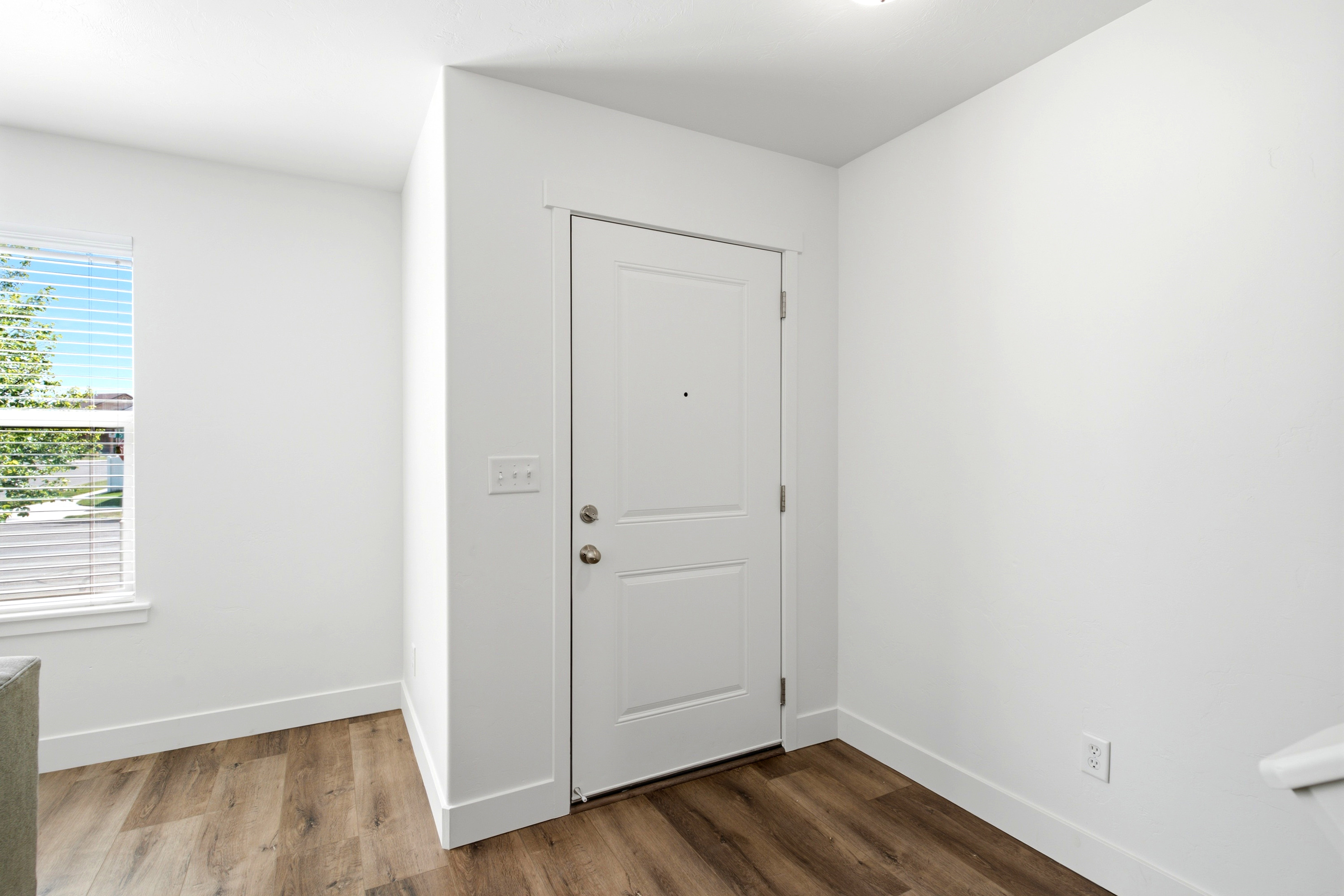 Entryway featuring a paneled door, wood-finish flooring, white walls, and a window with blinds