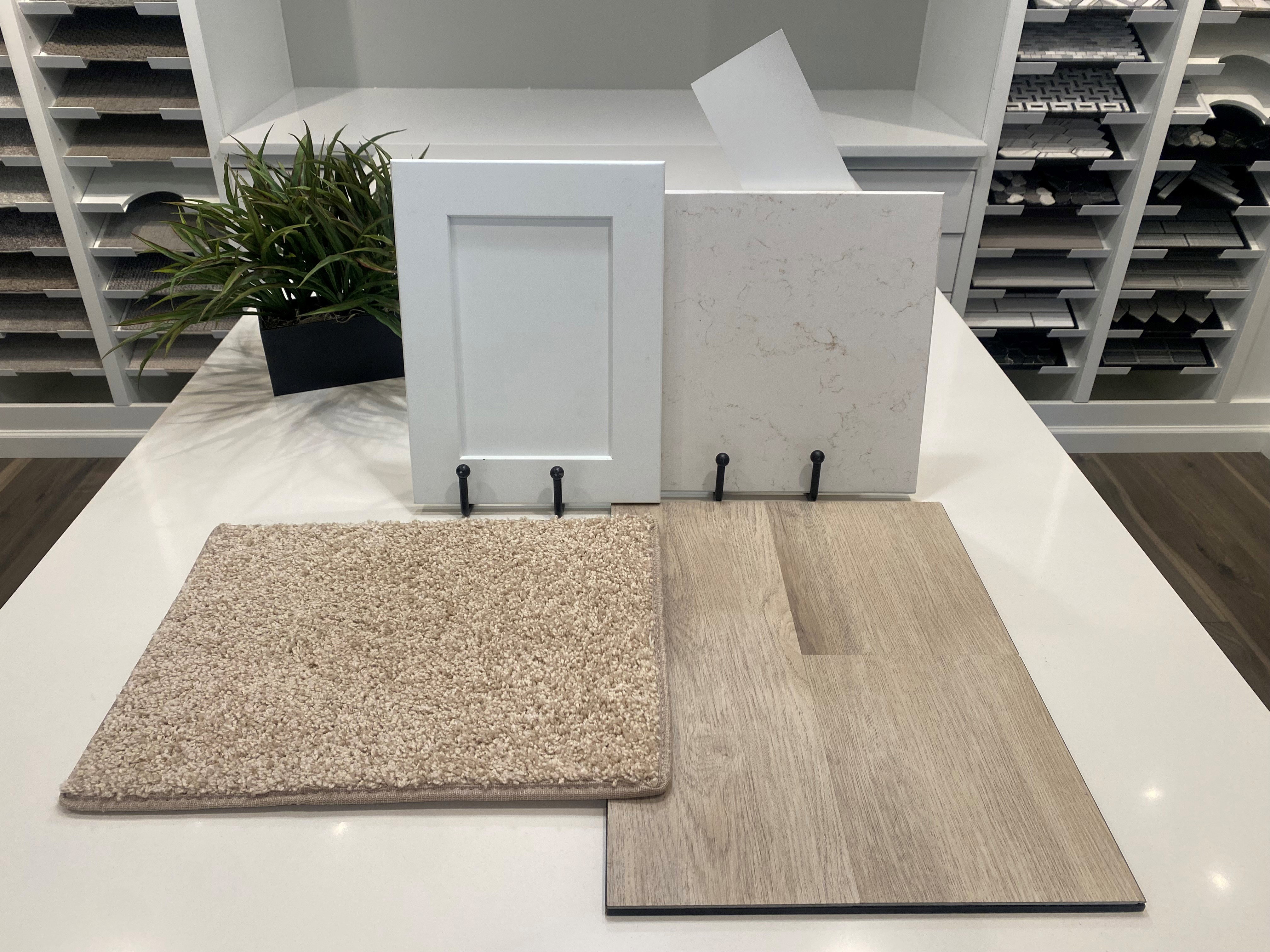 Design samples including white shaker cabinet door, quartz countertop slab, beige carpet swatch, and wood-finish flooring