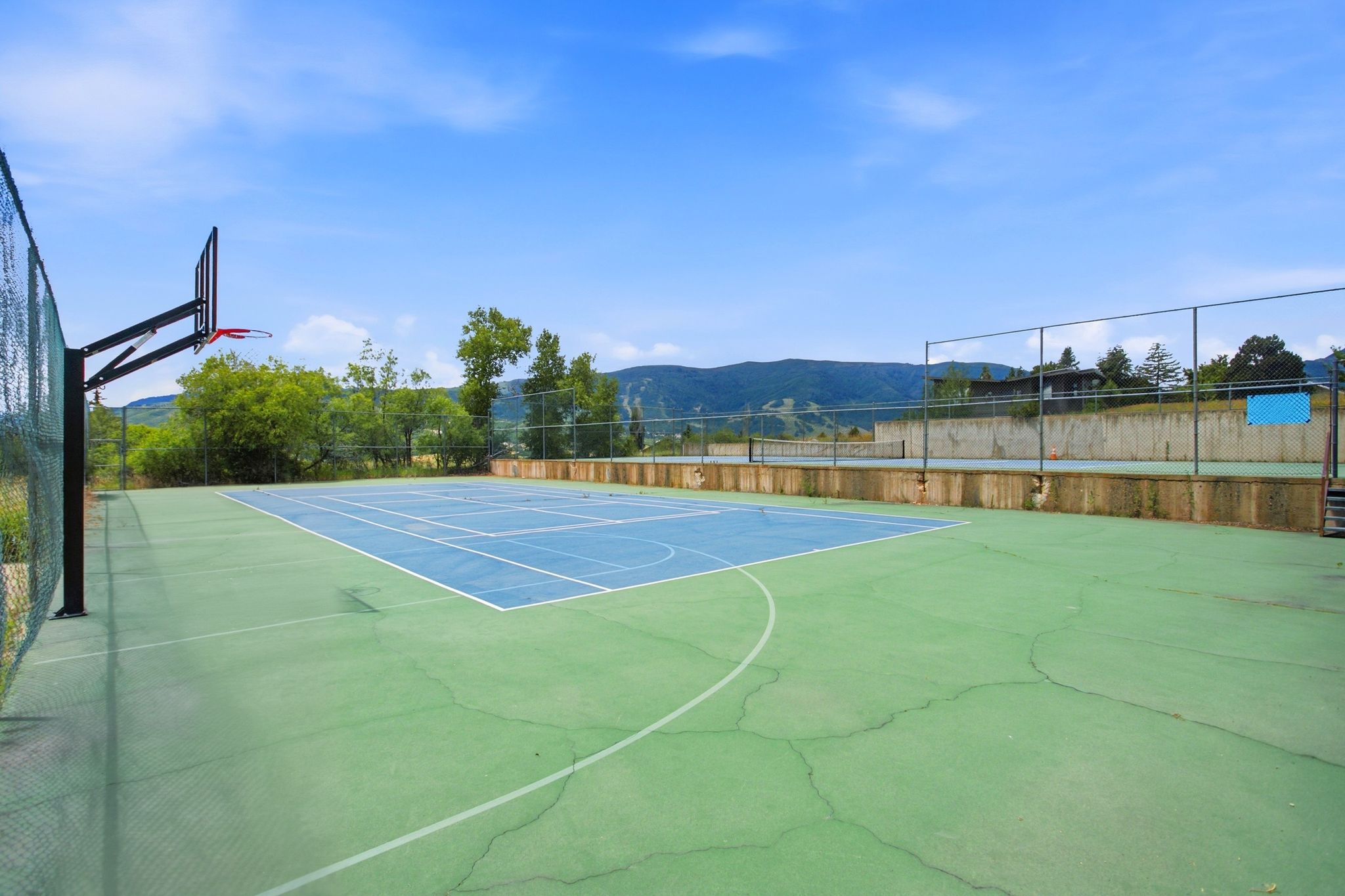 Multi-sport court featuring a basketball hoop, chain-link fencing, and a concrete retaining wall