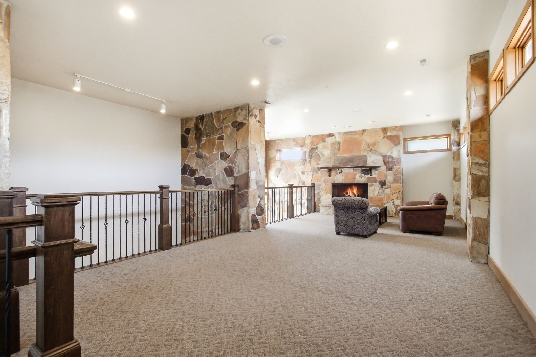 Spacious open loft featuring a stone-clad fireplace and hearth, wood-finish railing with wrought iron balusters, and recessed lighting