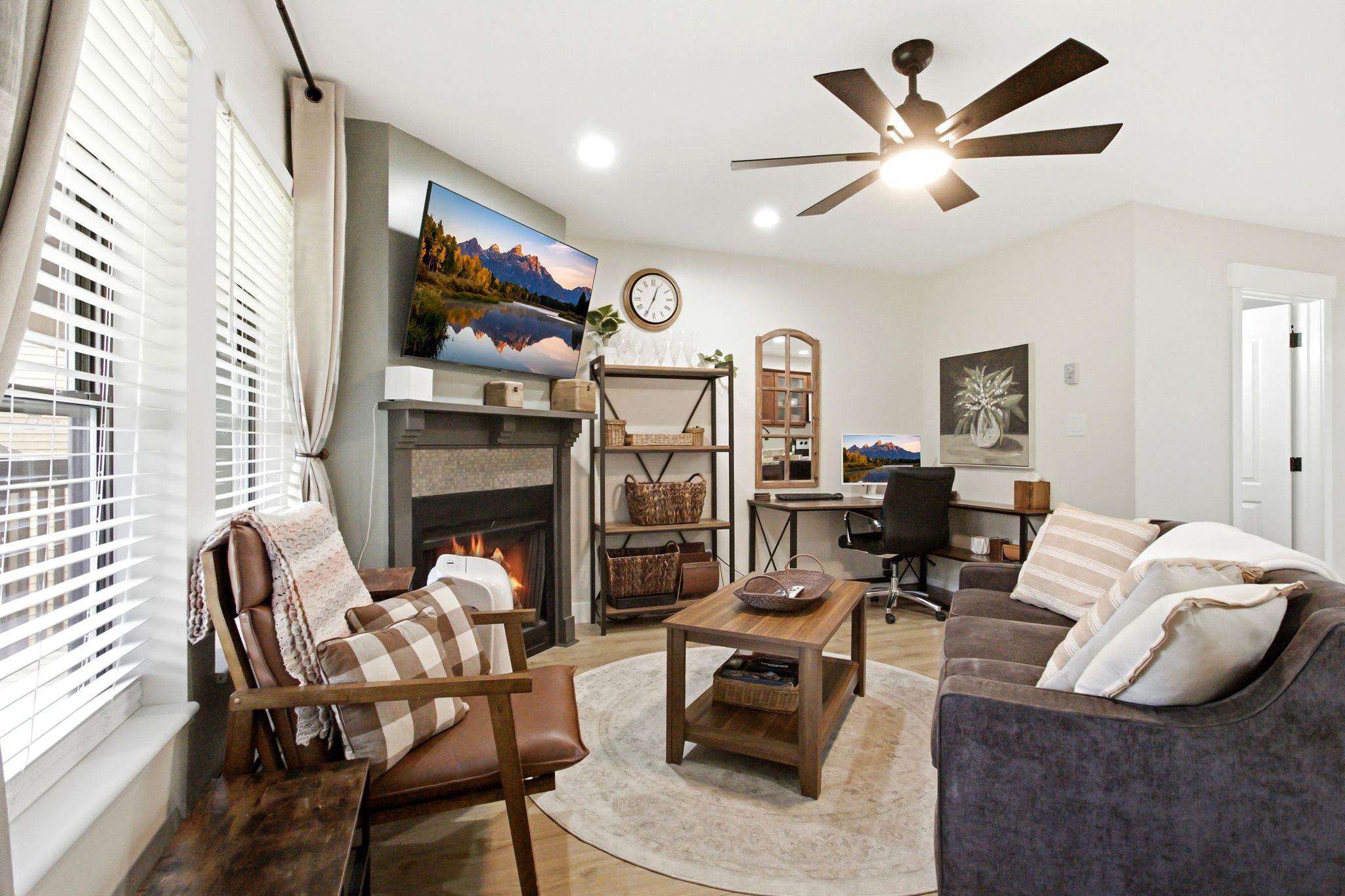 Living area featuring a fireplace with a stone surround and wood mantel, large windows with horizontal blinds, overhead ceiling fan with lighting, wood-finish flooring, and recessed lighting