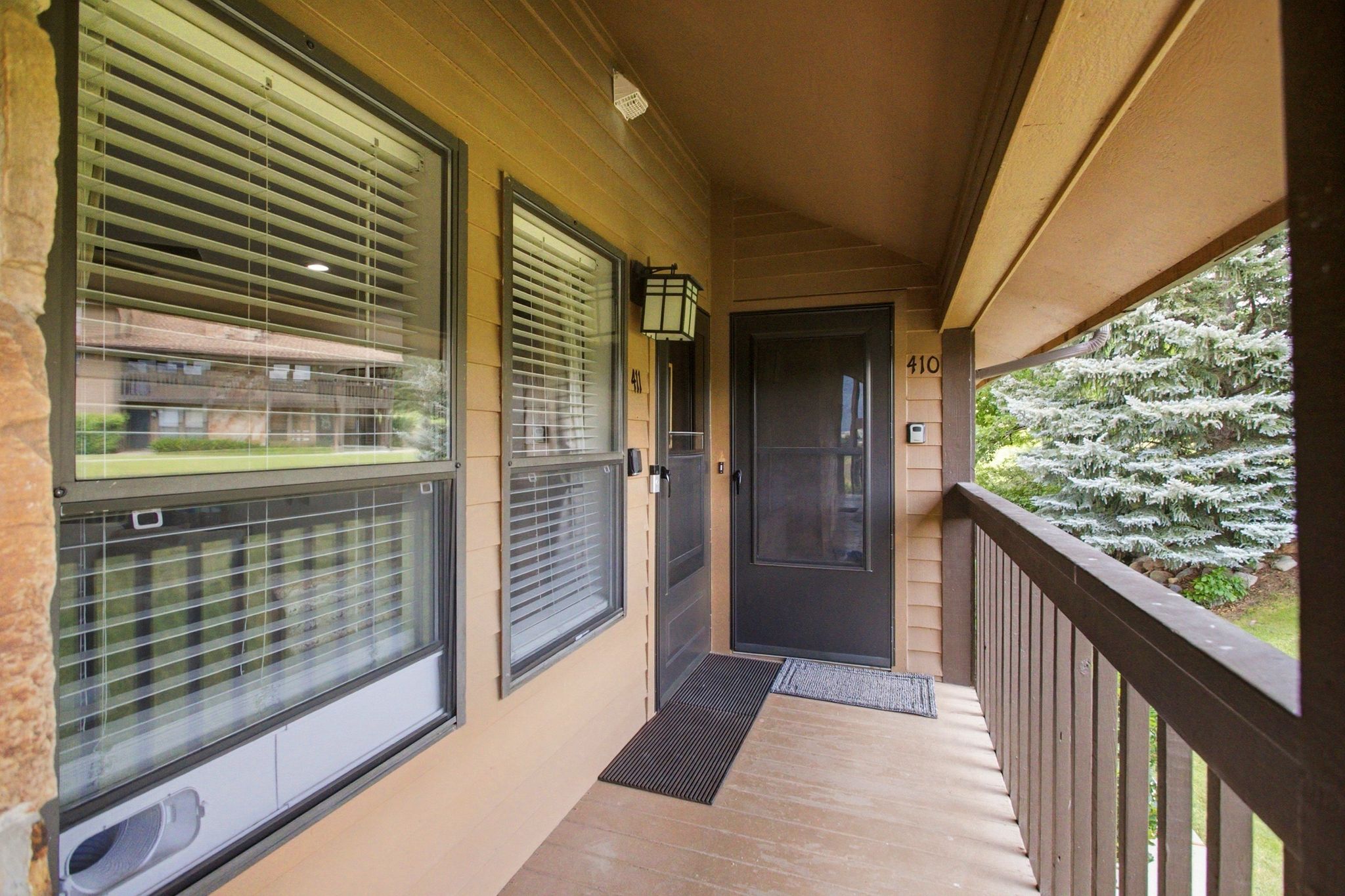 Covered porch entrance featuring a dark brown entry door with a screen, wood-finish siding, and an outdoor wall light fixture