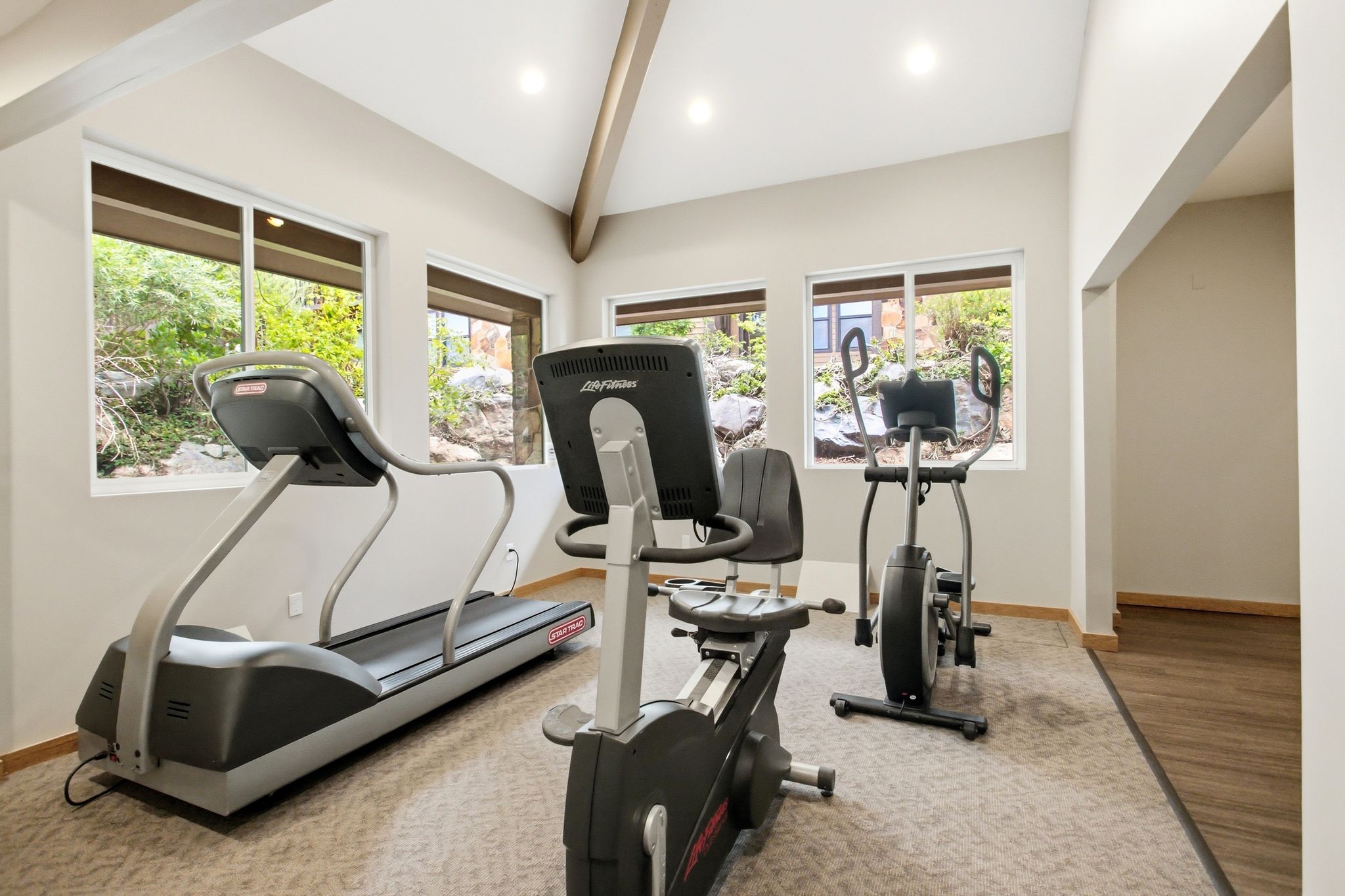 Dedicated exercise space featuring multiple windows, vaulted ceilings with exposed wood beams, recessed lighting, and carpeted flooring