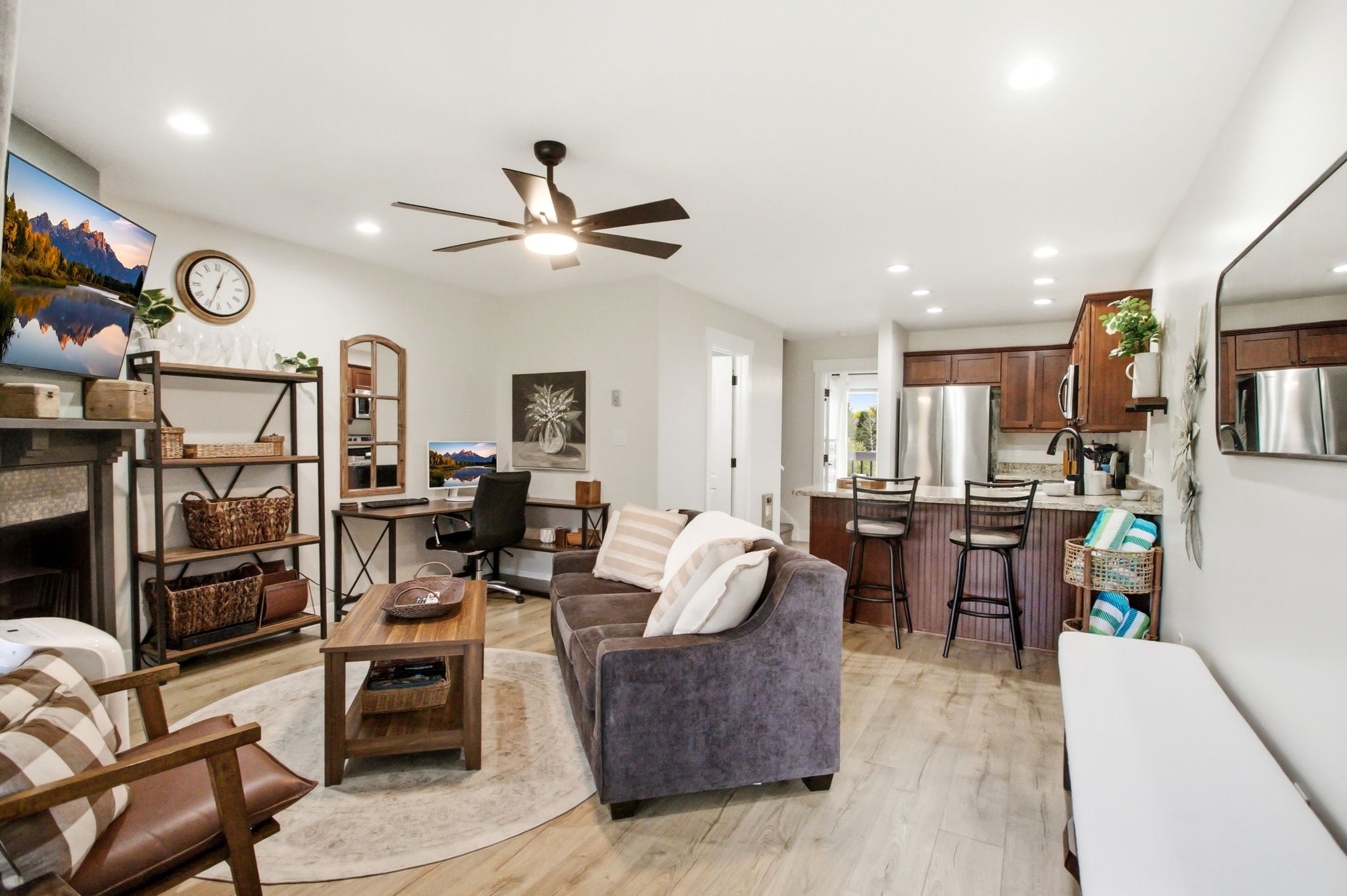 Open-concept living area featuring light wood-finish flooring, recessed lighting, a ceiling fan, a kitchen with dark wood cabinetry and stainless steel appliances, and a breakfast bar