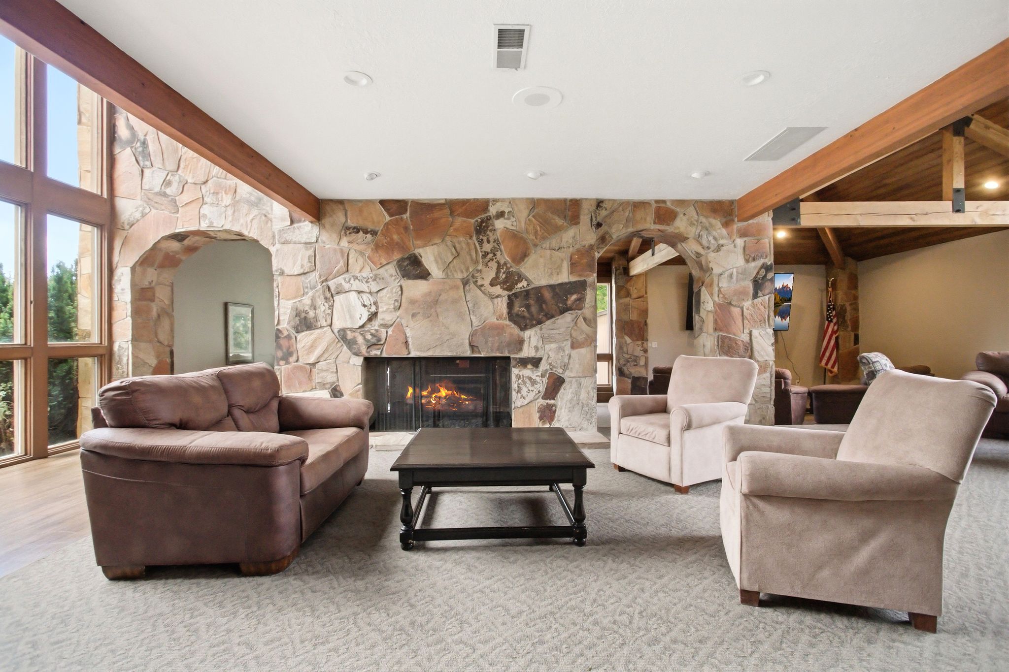 Spacious living area featuring a floor-to-ceiling stone fireplace, large archways, and exposed wood beams