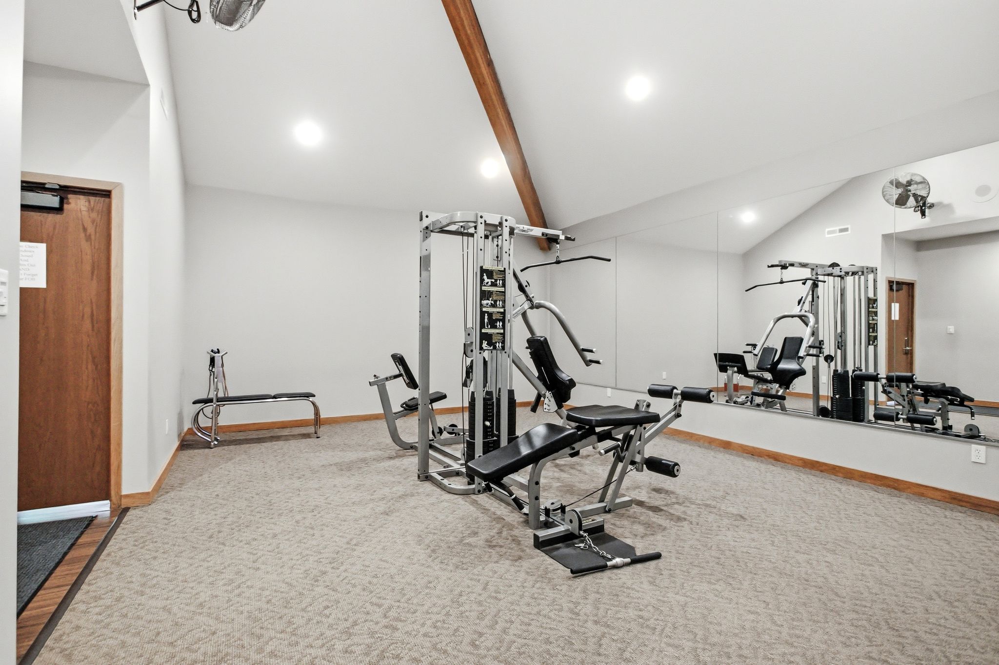 Fitness area featuring neutral-toned carpet, a vaulted ceiling with exposed wood beam, recessed lighting, and a full-length mirrored wall