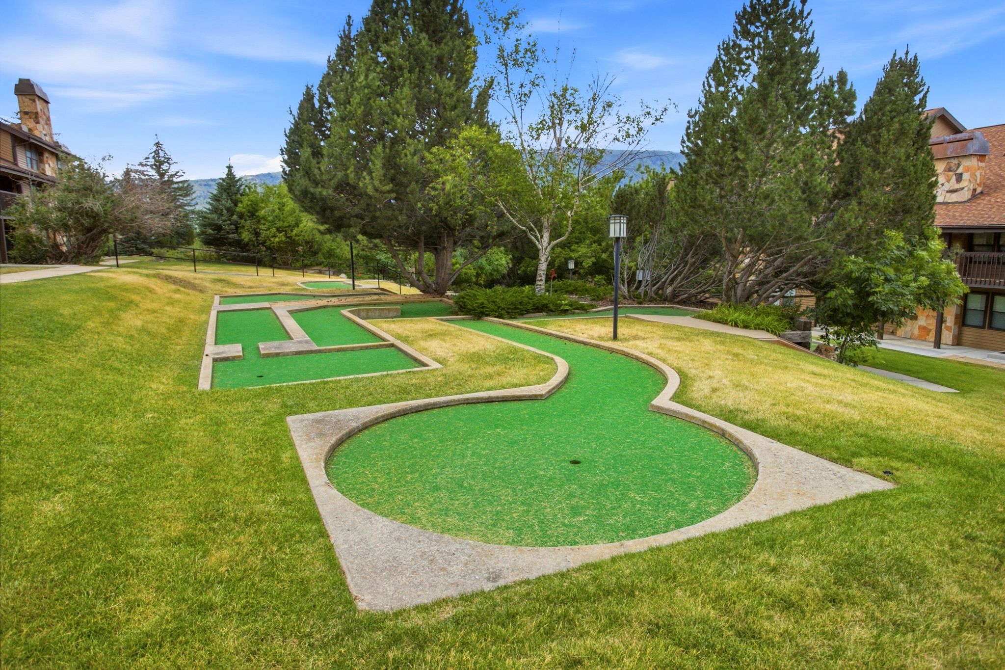 Miniature golf course featuring multiple holes with artificial turf and concrete borders, set within a landscaped grassy area