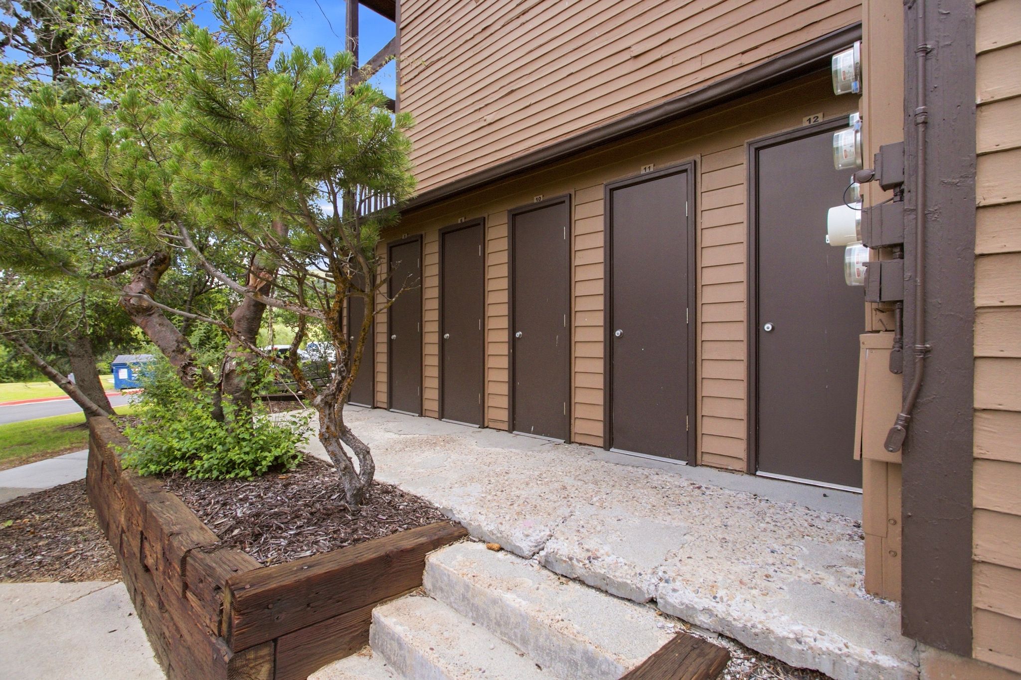 Exterior storage units featuring wood siding, concrete walkway, and landscaped retaining wall