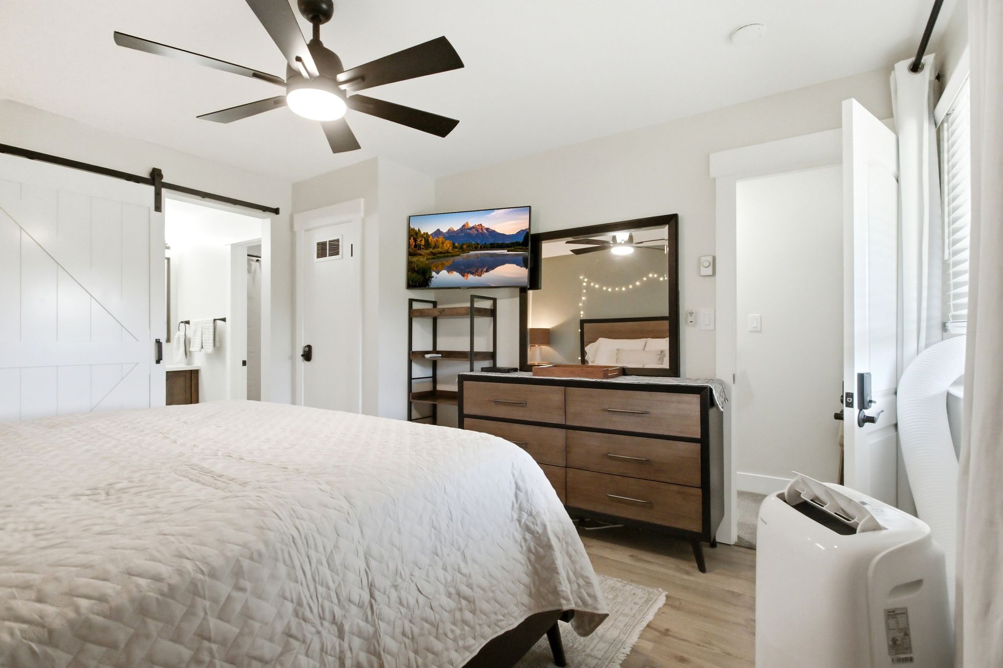 Bedroom featuring wood-finish flooring, a ceiling fan with integrated lighting, a sliding barn door, and a built-in window with horizontal blinds