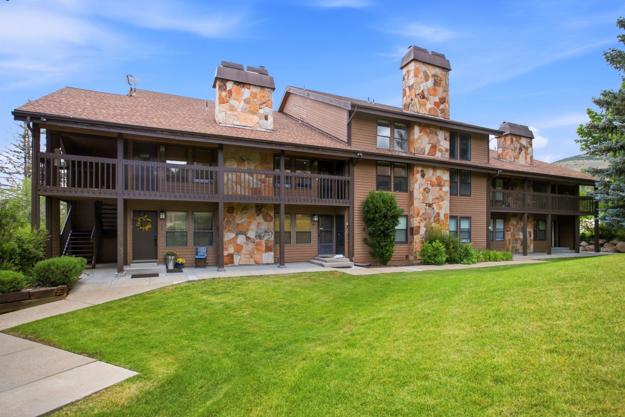 Multi-unit property featuring stone accents, dark wood siding, multiple private balconies, ground-floor patios, and prominent stone chimneys